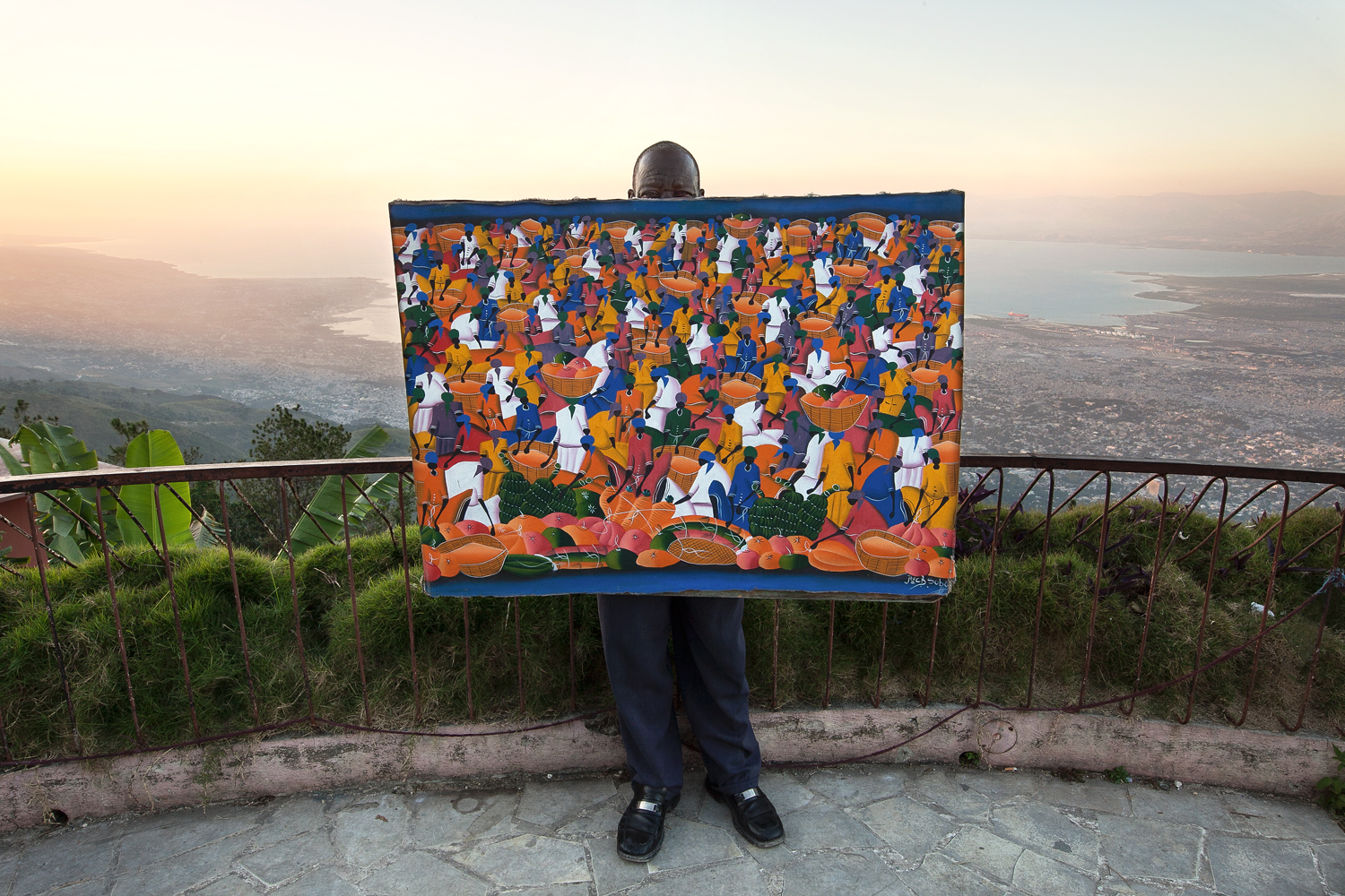  A local artist proudly holds his latest masterpiece depicting a traditional scene from the Haitian culture. He sells his work at a popular road-side lookout known for its view of Port-au-Prince. 