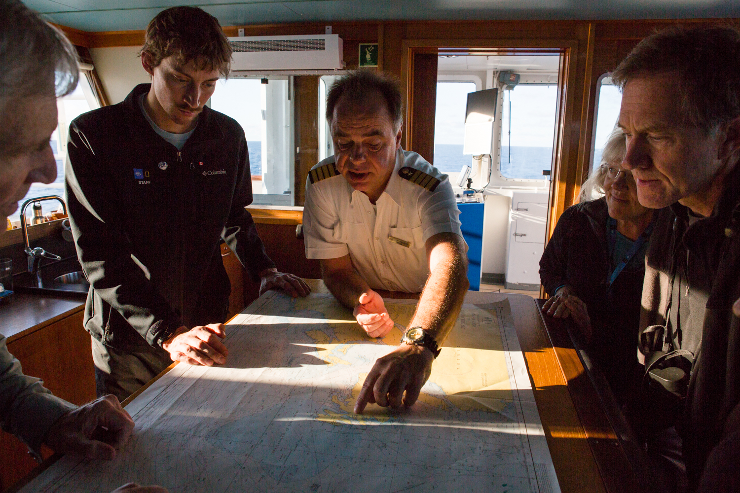  The captain aboard the National Geographic Explorer expedition vessels point out a sailing route on paper charts. 