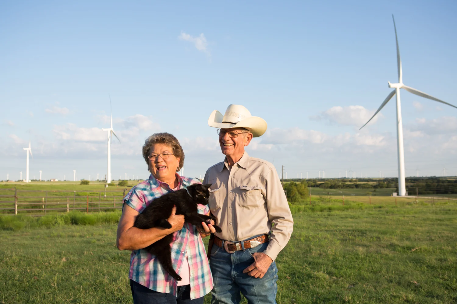 Charles and Jane pose for a portrait with their cat Stinky in their property's pasture.
