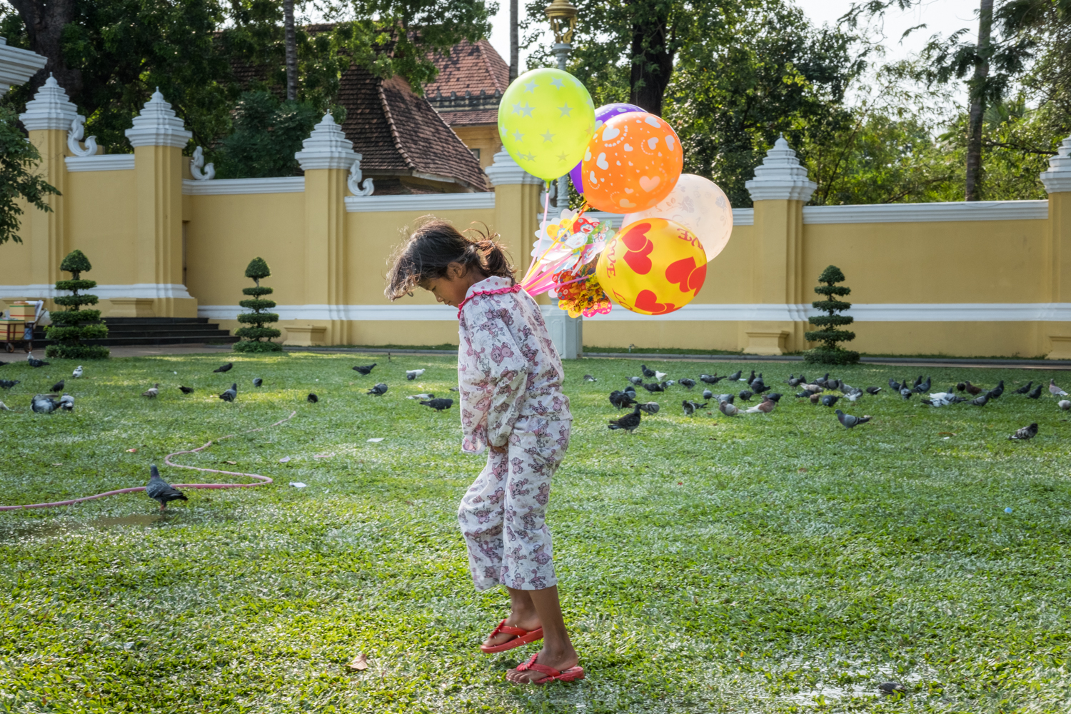  A young girl selling balloons walks through a wet and muddy field outside the palace in Phnom Penh, Cambodia. 