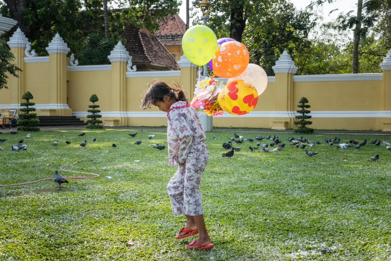 A young girl selling balloons walks through a wet and muddy field outside the palace in Phnom Penh, Cambodia.