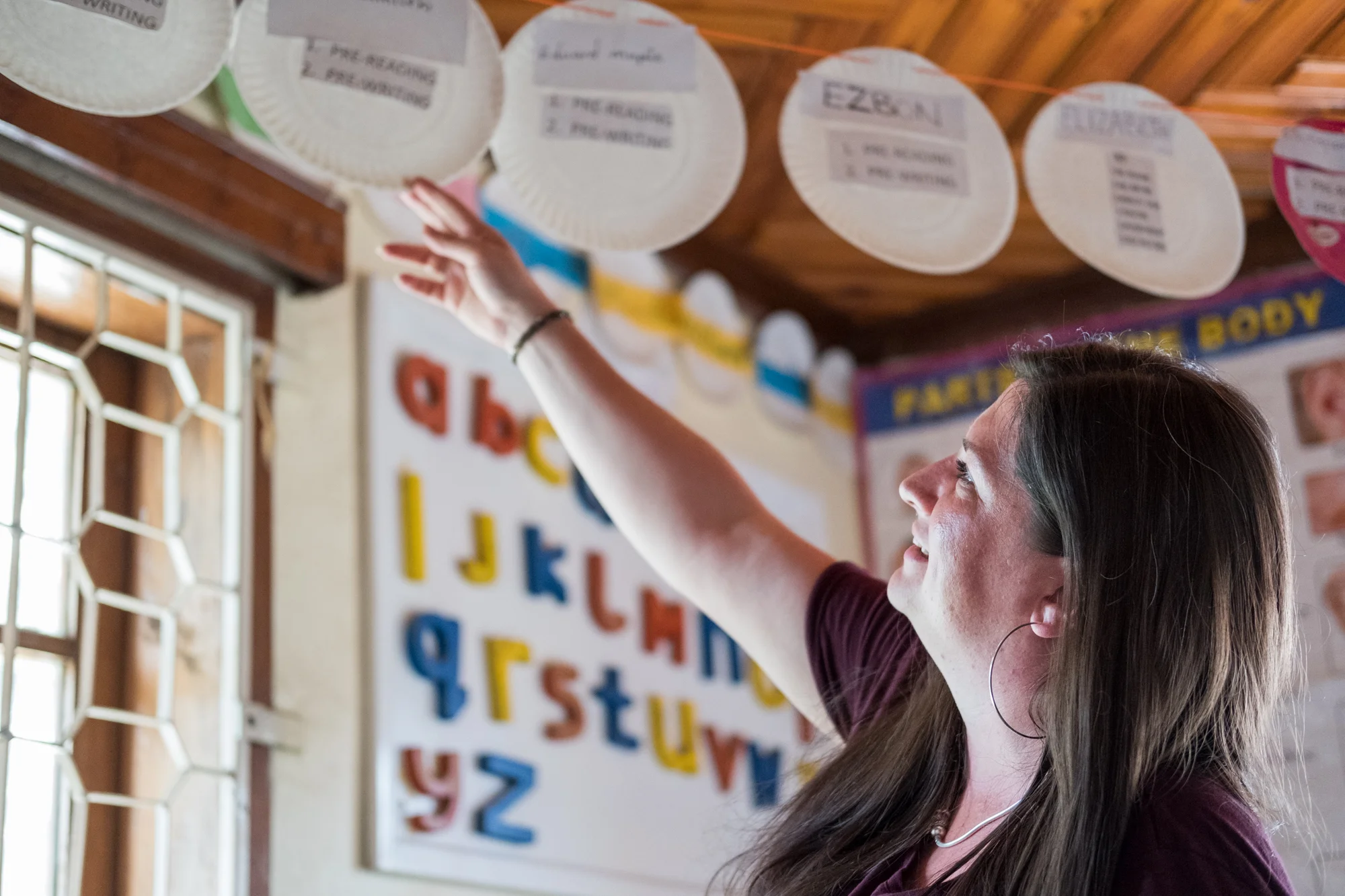 Holly looks at plates hanging in a classroom at Child Support Tanzania. Each plate is assigned to one student and has a list of his/her current learning activities.