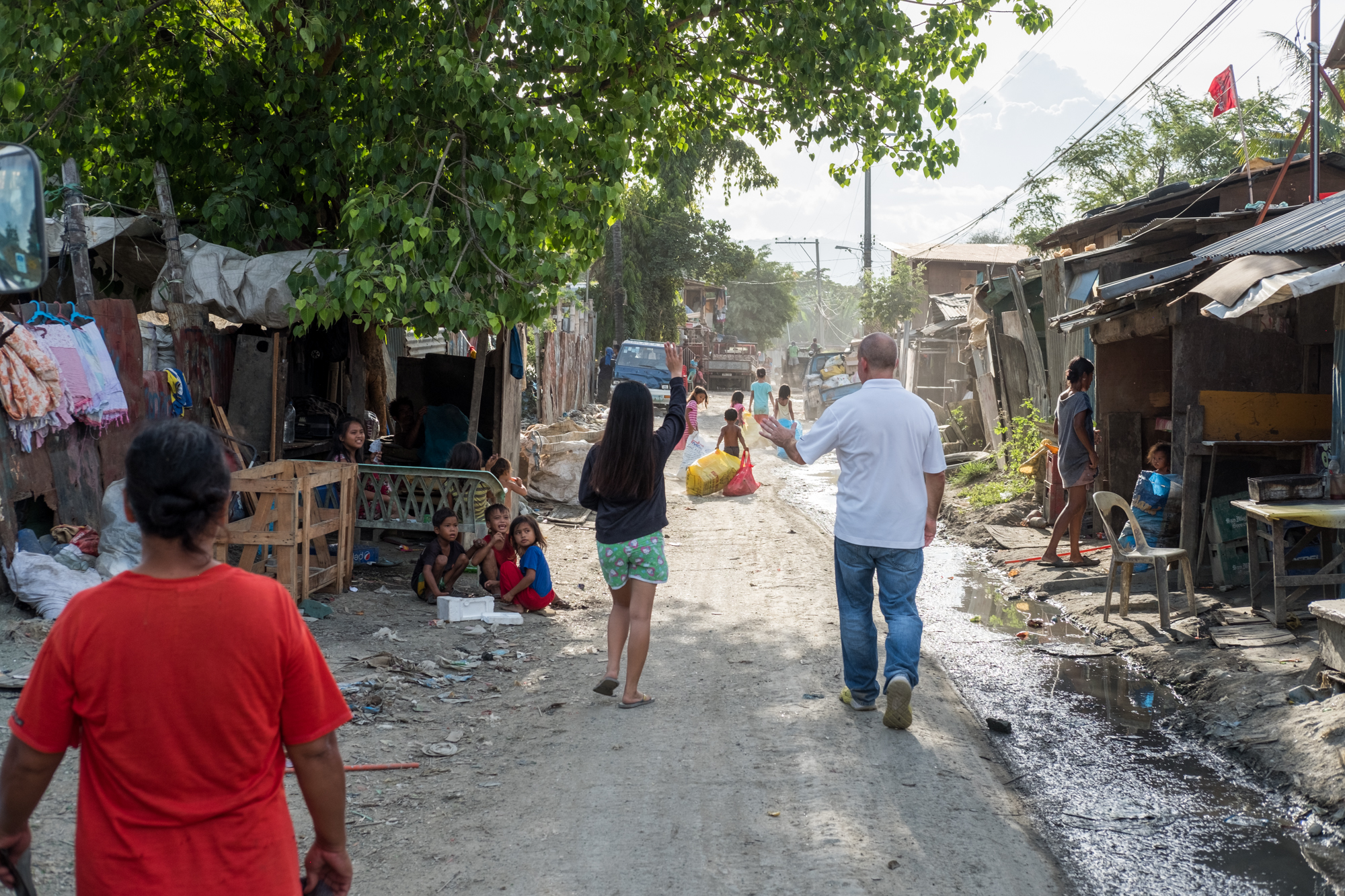  Frank Becker (right) walks with Marie Perly Anciano (left) on a road near the Mandaue Dump Site in Cebu, Philippines. Frank visits the dumpsites daily, and Marie is one of the many children that Frank has helped by donating school supplies and offer