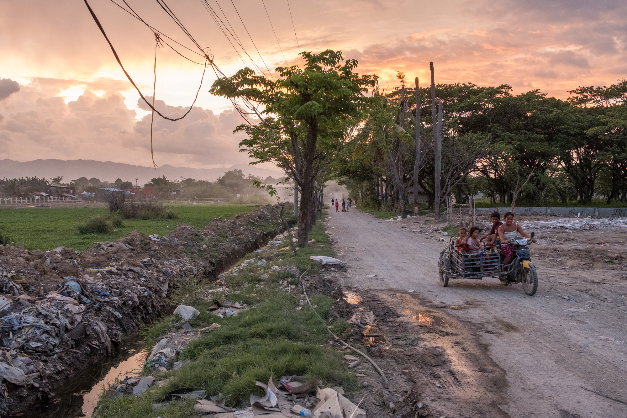  A colorful sunset illuminates the sky as people drive along a road near the Mandaue Dump Site in Cebu, Philippines. 