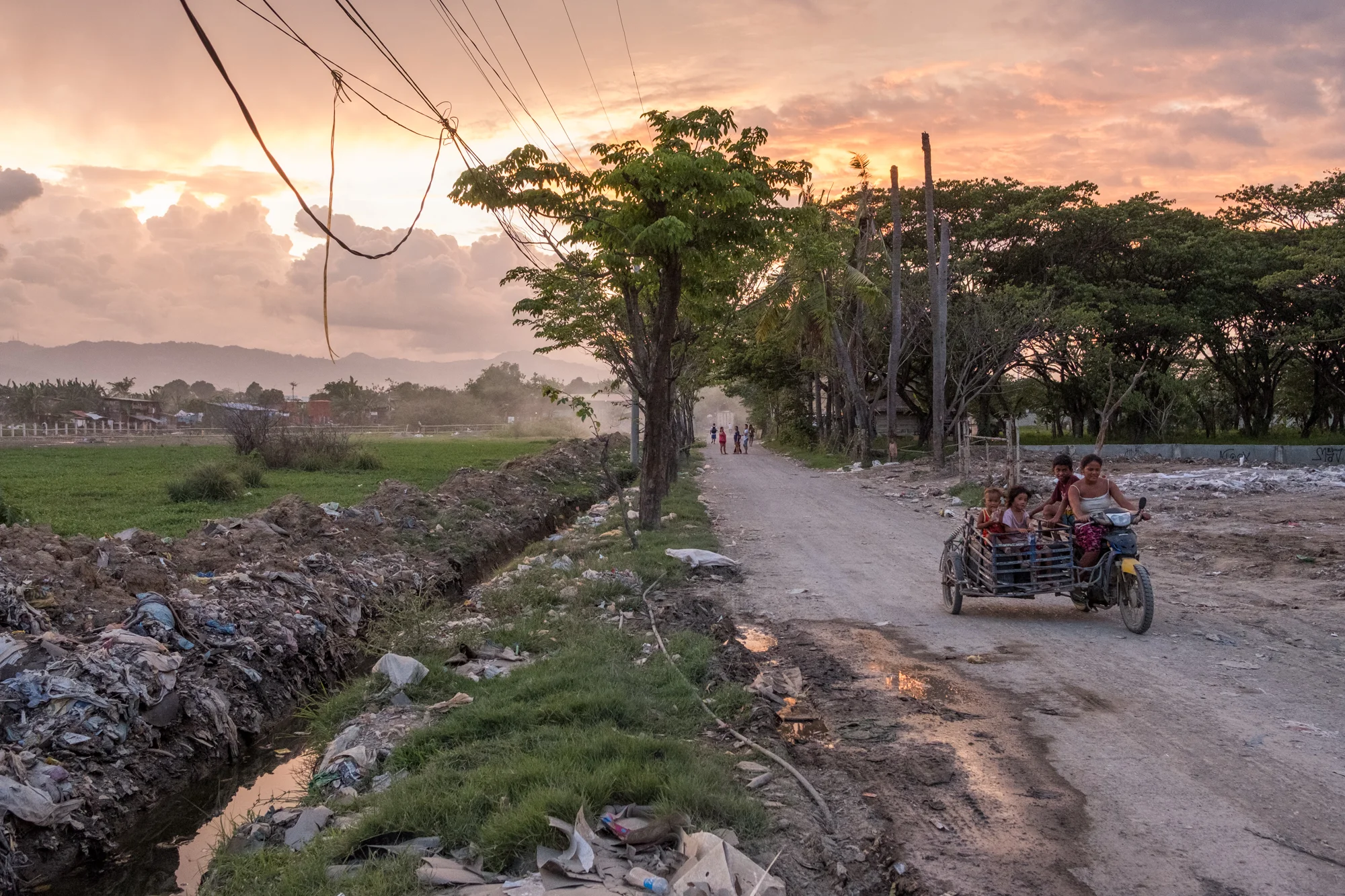 A colorful sunset illuminates the sky as people drive along a road near the Mandaue Dump Site in Cebu, Philippines.