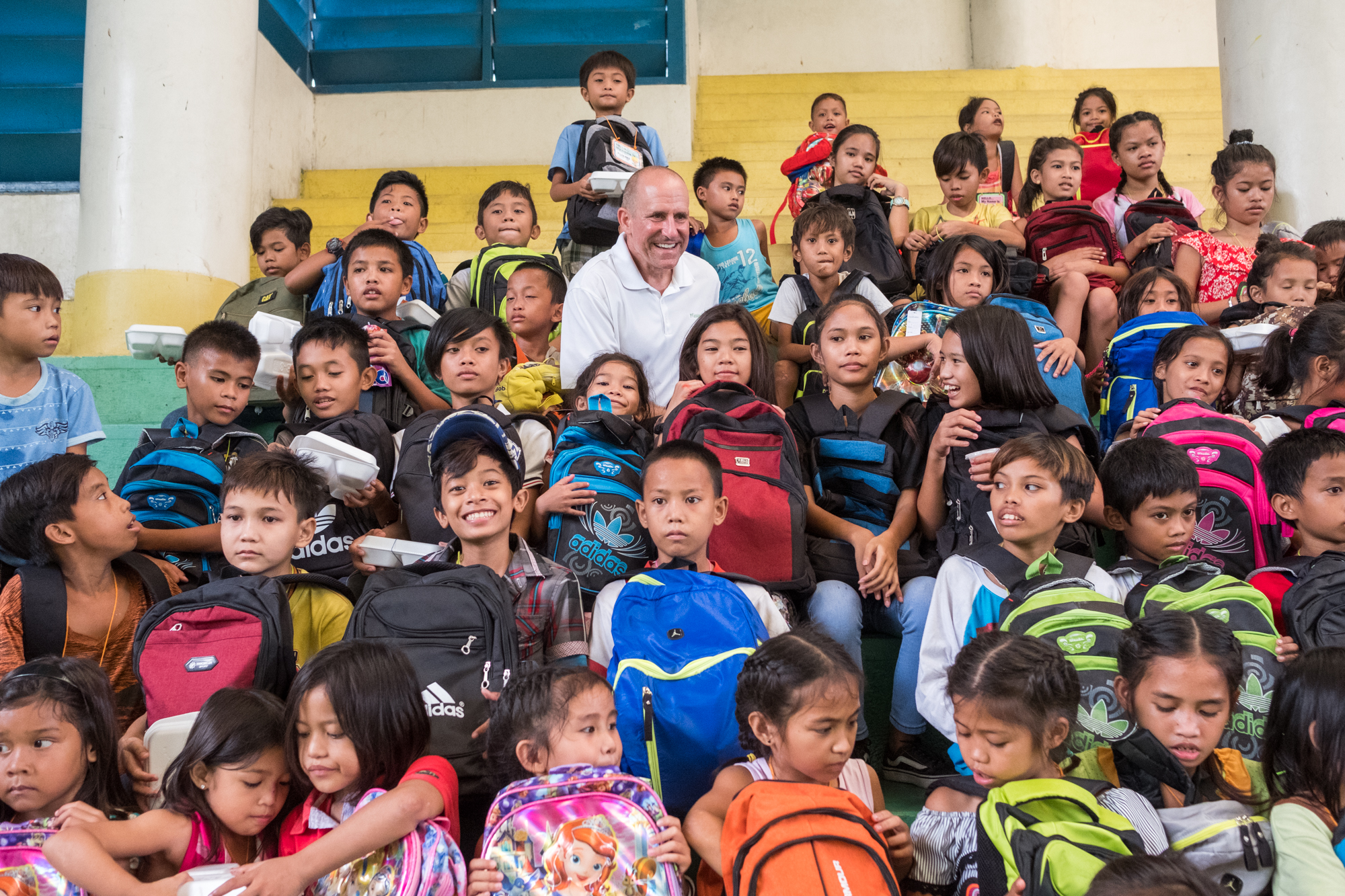  Frank Becker (top center) poses for a picture with students who received new backpacks filled with school supplies at a community-giving event in Cebu, Philippines. Because of Frank’s efforts, hundreds of children received supplies during this sabba