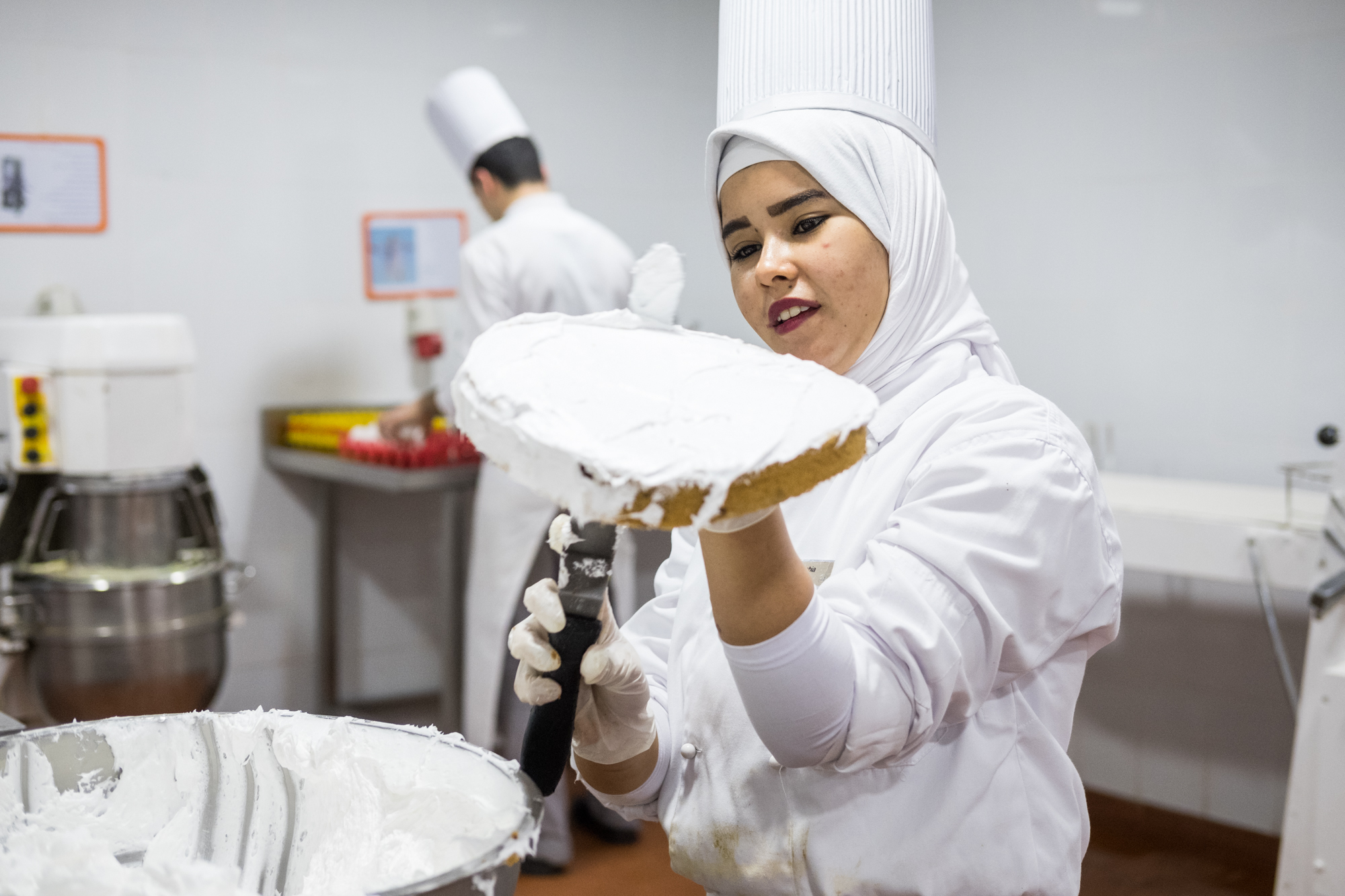 Amira, a trainee in the Kitchen/Pastry Section, prepares a fresh cake and frosting.