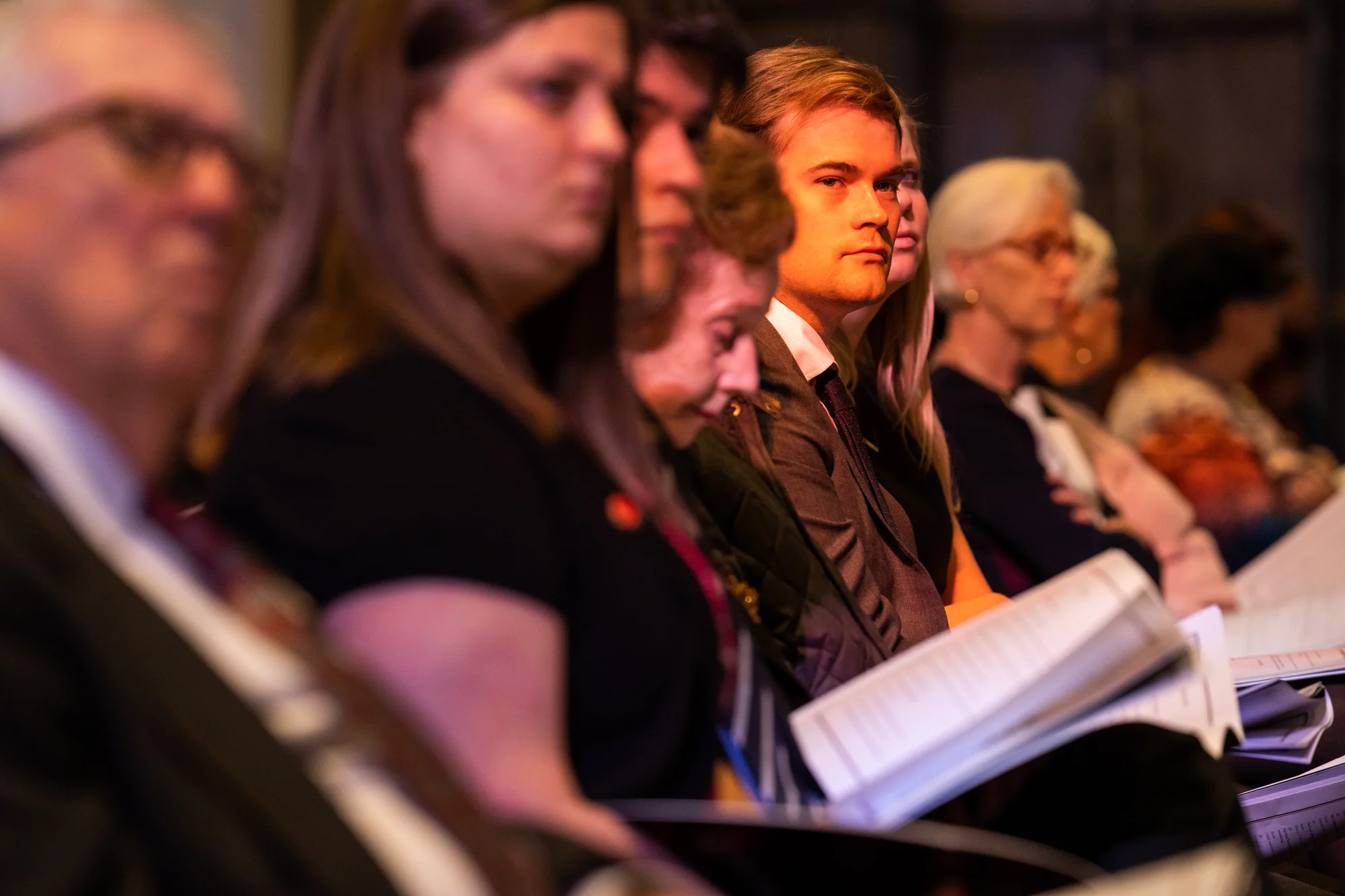 A guest is illuminated by light coming through a stained-glass window while watching the service.