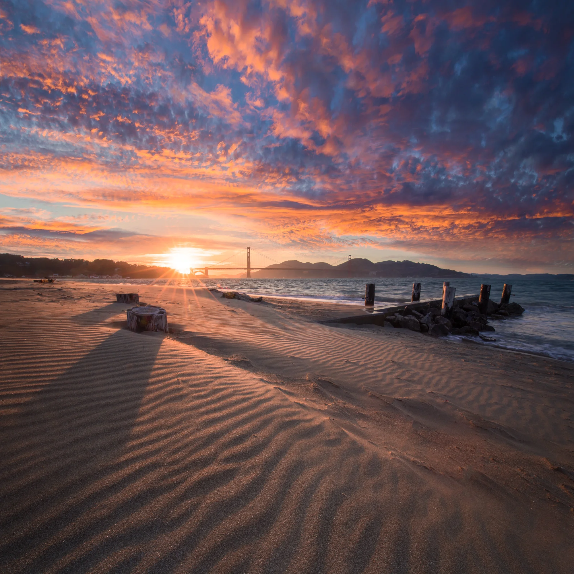 **Crissy Field Textures**

Sunset over San Francisco Bay with the Golden Gate Bridge in the distance—wind-sculpted sand ripples at Crissy Field Beach creating intricate patterns in the foreground.

Crissy Field offers a different perspective on the G