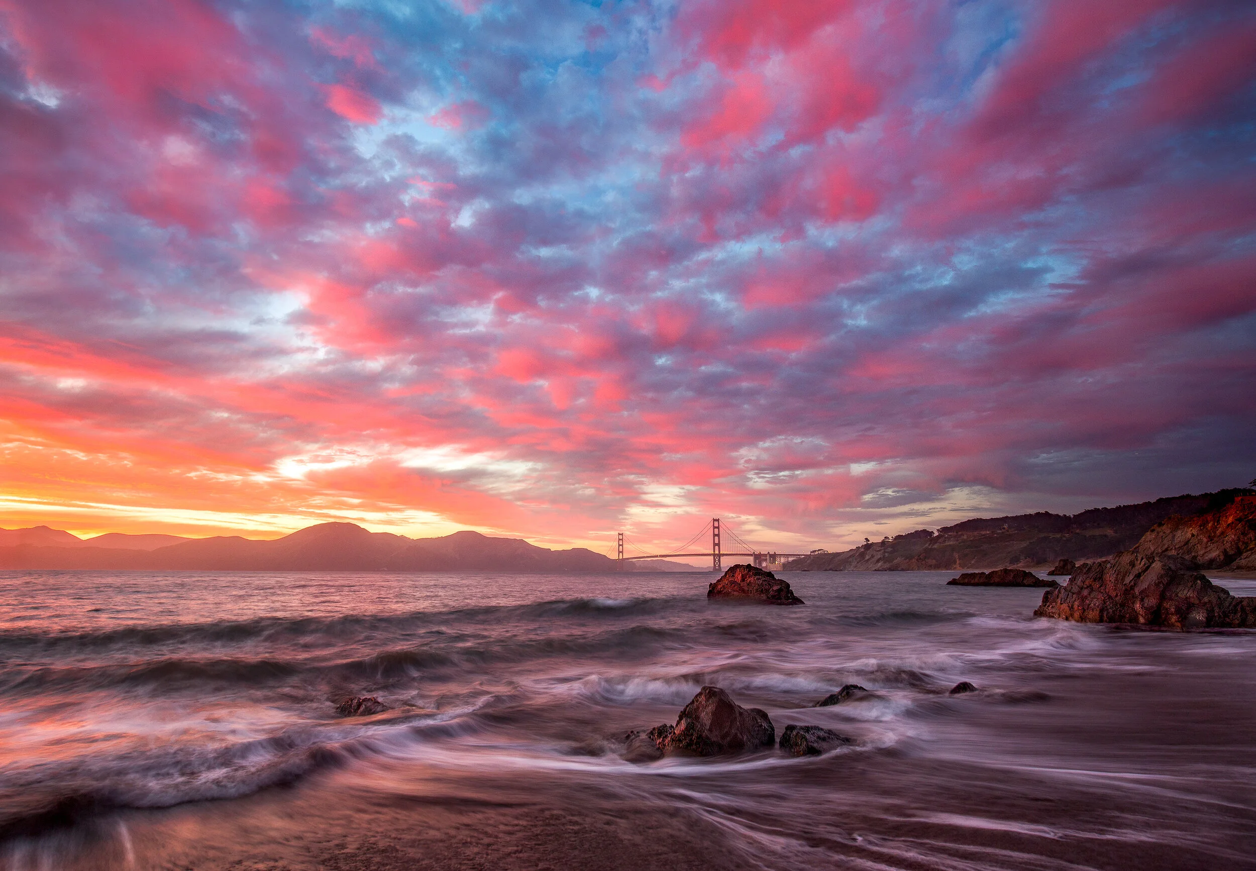**China Beach Sunset**

The Golden Gate Bridge from China Beach at sunset—waves receding around boulders, dramatic clouds painting the sky.

China Beach offers one of the most intimate perspectives on the Golden Gate Bridge. Unlike the elevated viewp
