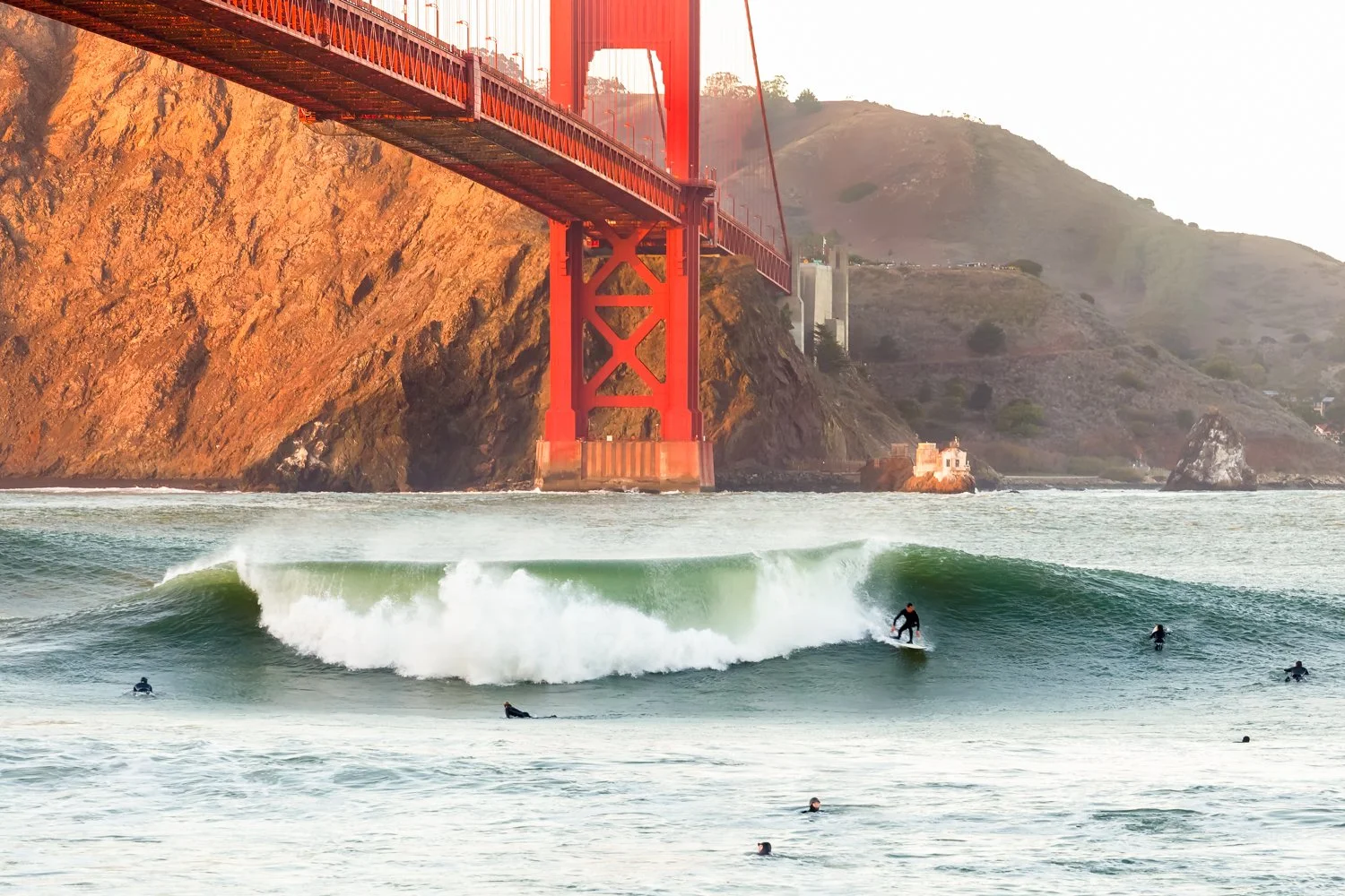 **Surfing Under the Golden Gate**

Pure San Francisco living—where world-class surfing meets iconic architecture.

I positioned myself to capture surfers riding waves beneath the Golden Gate Bridge during golden hour. This is the intersection of two 