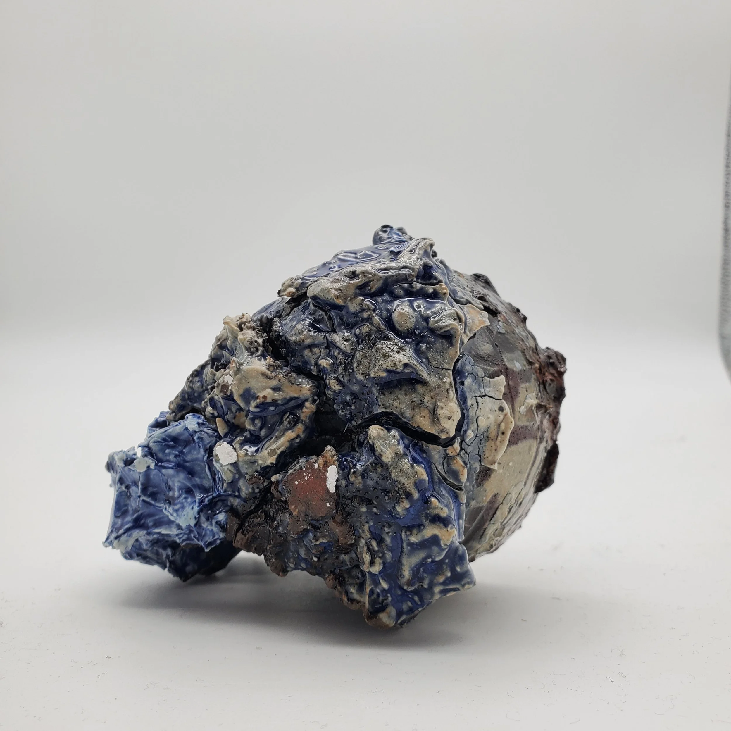 A rough, crumpled rock with dark blue, beige, grey, and brown colors on a plain white background.