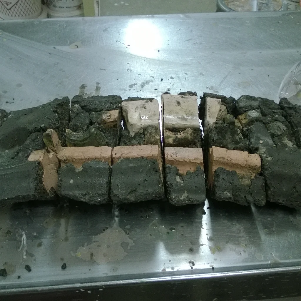 A segmented brick and concrete block structure on a metallic surface with solder and debris, possibly part of a repair or construction project.