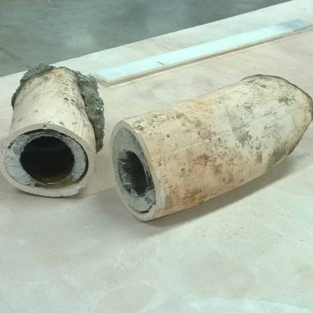 Two corroded and dirty ceramic pipes lying on a white surface, with a gray background.