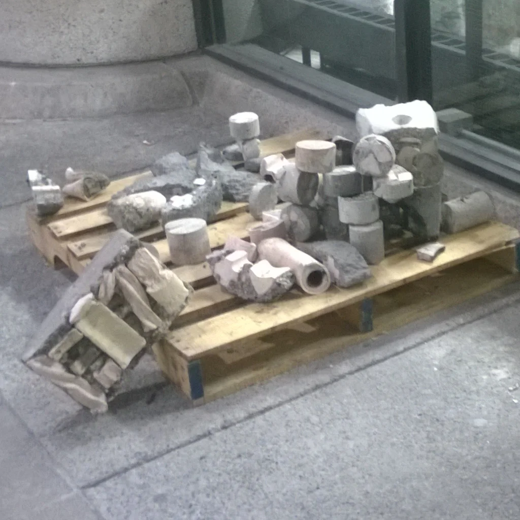 Collection of broken concrete and pipe fragments placed on a wooden pallet outside a building.