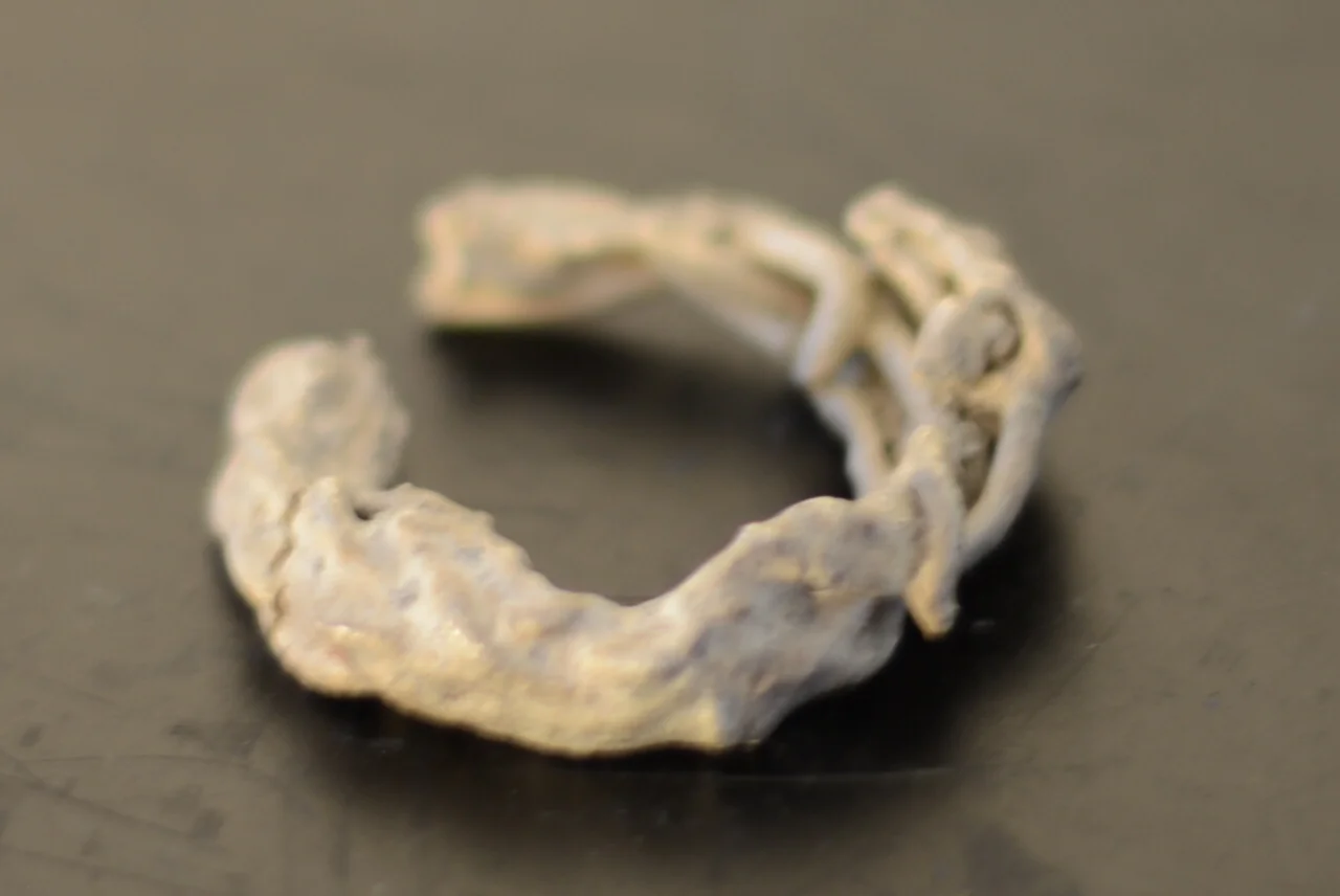 A weathered, irregularly shaped metal ring, possibly a piece of jewelry or an artifact, placed on a dark surface.