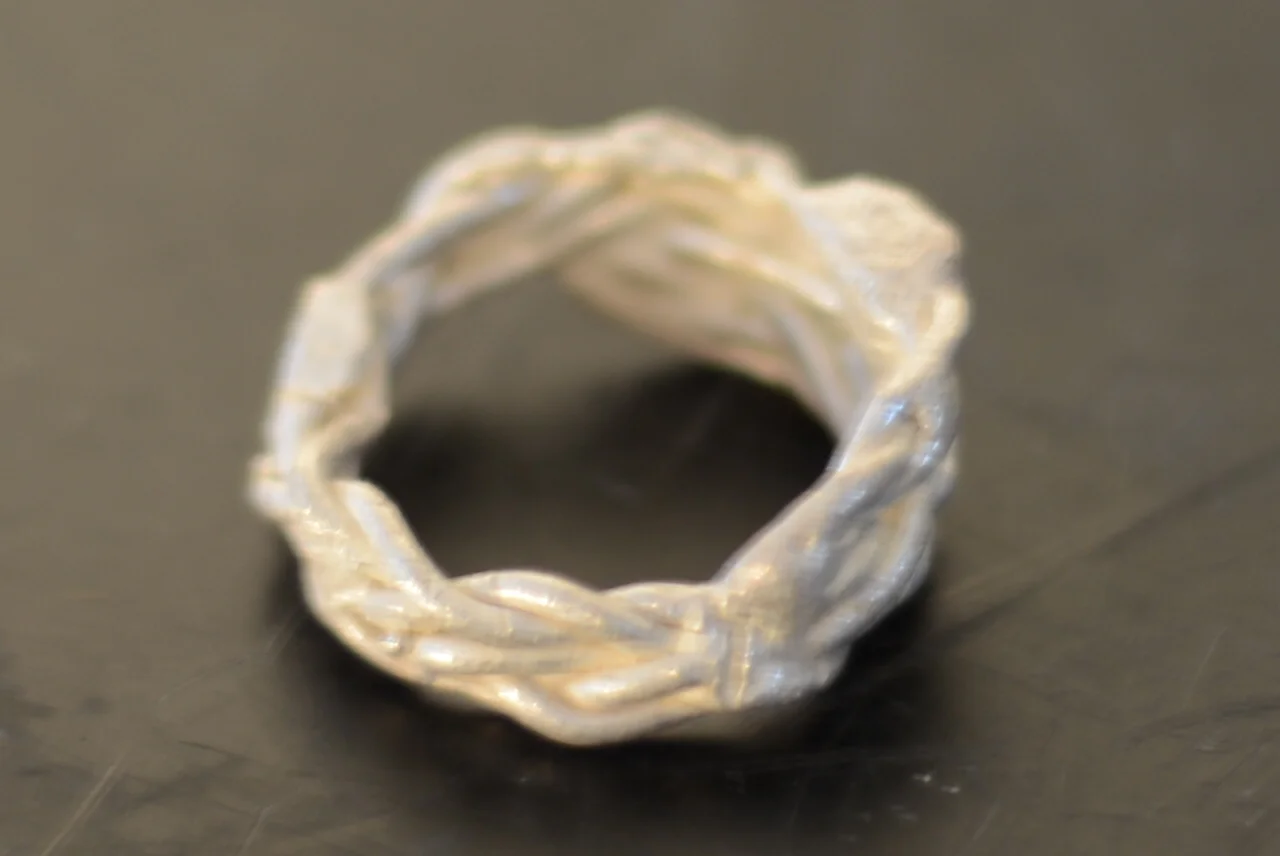 Close-up of a silver ring with a twisted, textured design on a dark surface.