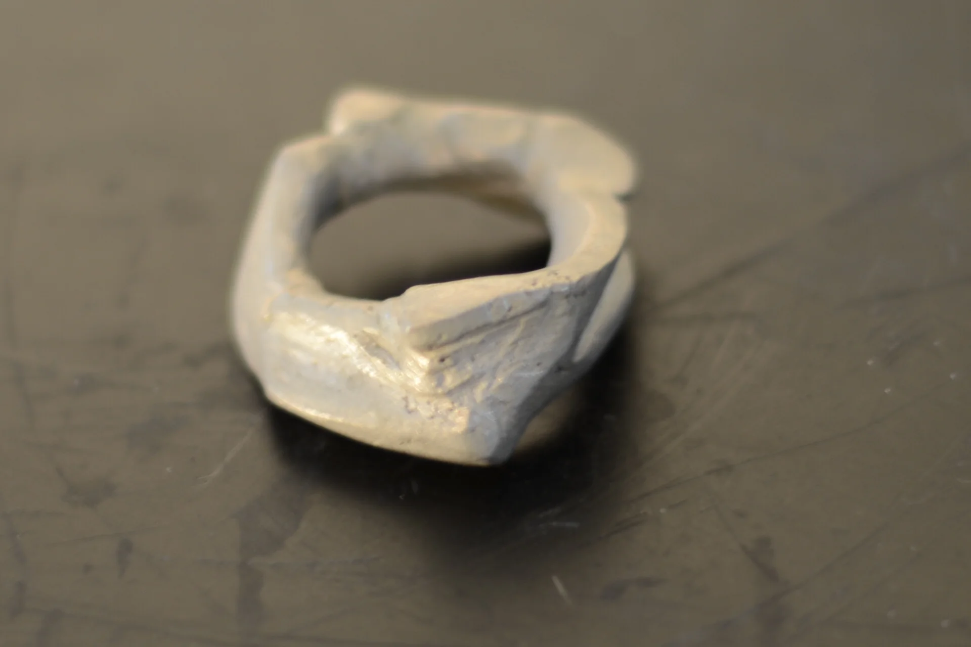 A silver ring with an irregular, rugged design placed on a dark surface.