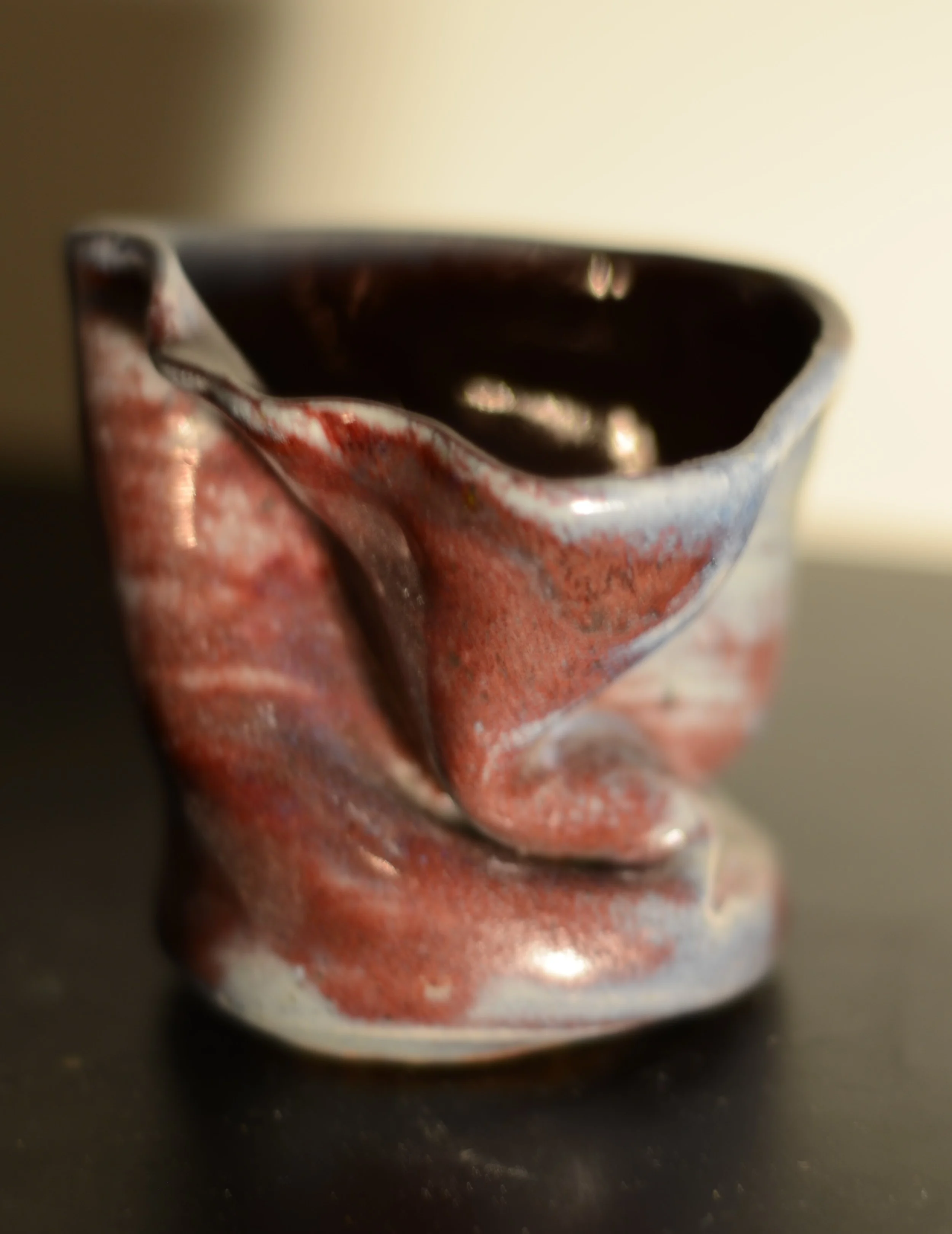 Close-up of a ceramic cup with an abstract red and white glaze, filled with a dark liquid, on a dark surface.