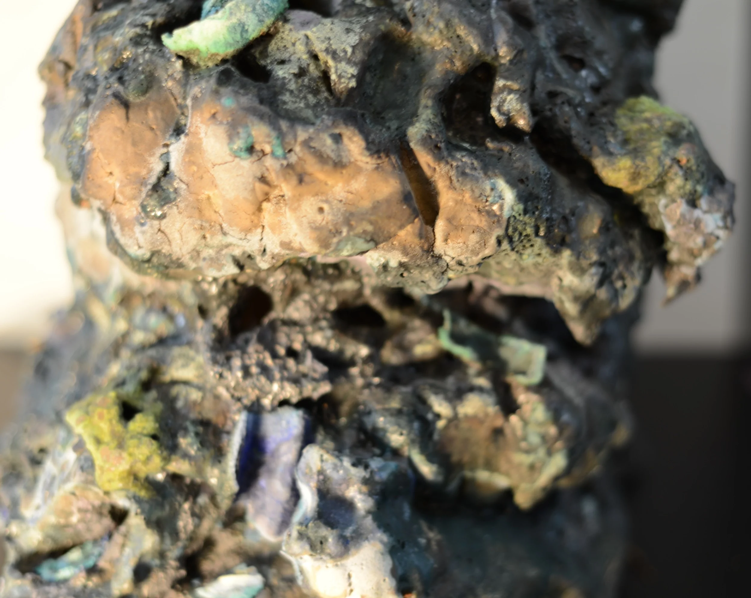 Close-up of a rough textured, multicolored exterior with patches of black, green, and brown, resembling a mineral or rock formation.