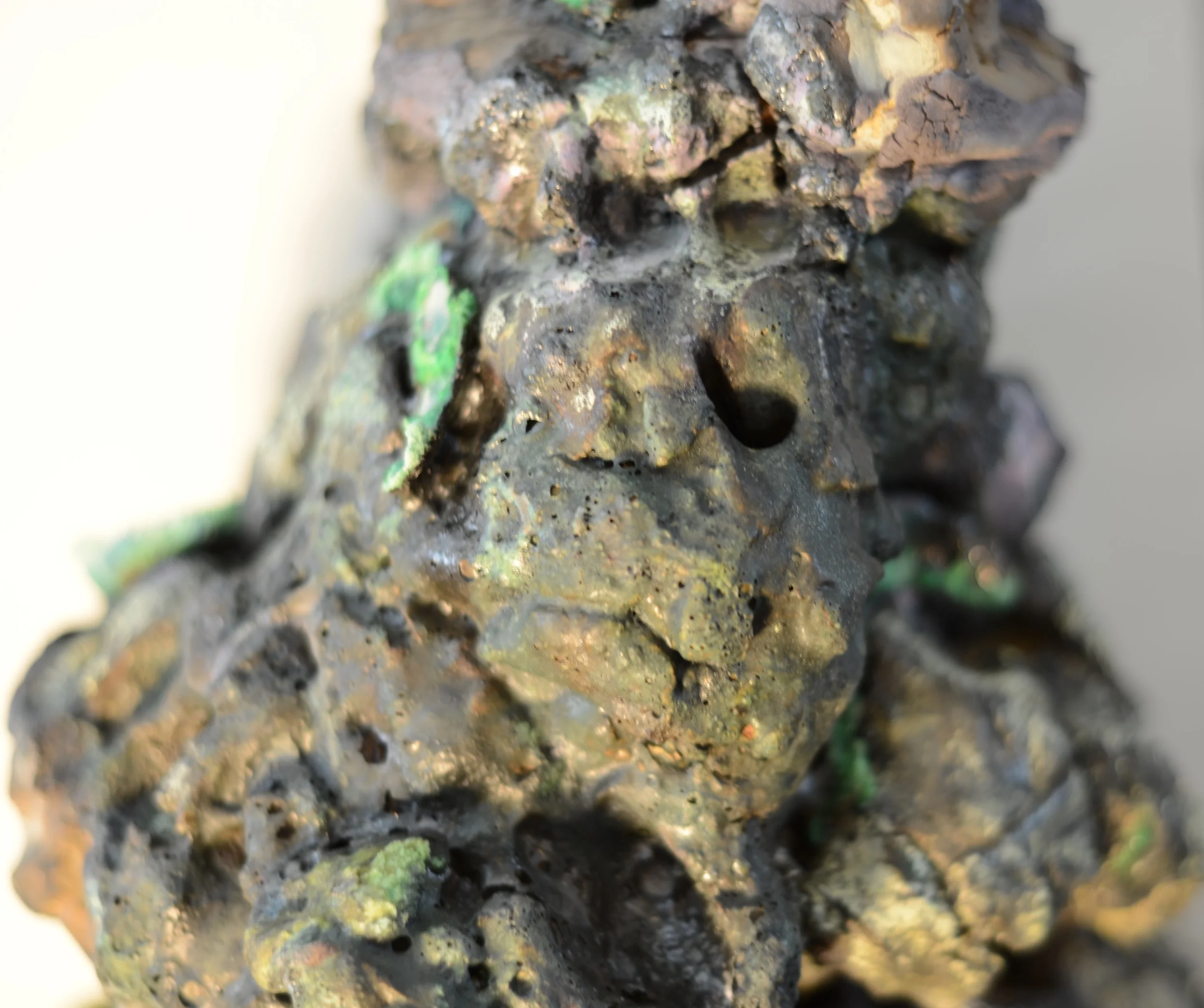 Close-up of a textured metallic sculpture of a face with green accents.