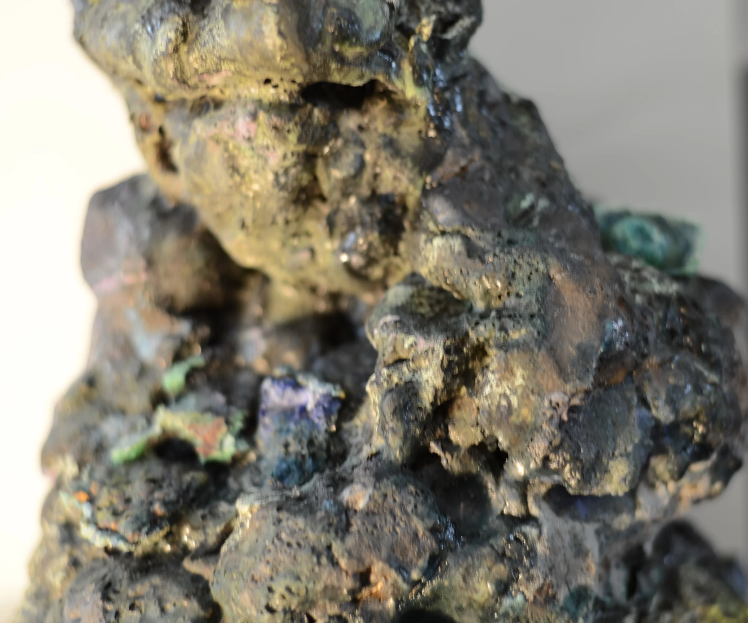 Close-up of a rough, dark, and textured stone surface with hints of colorful minerals embedded within.