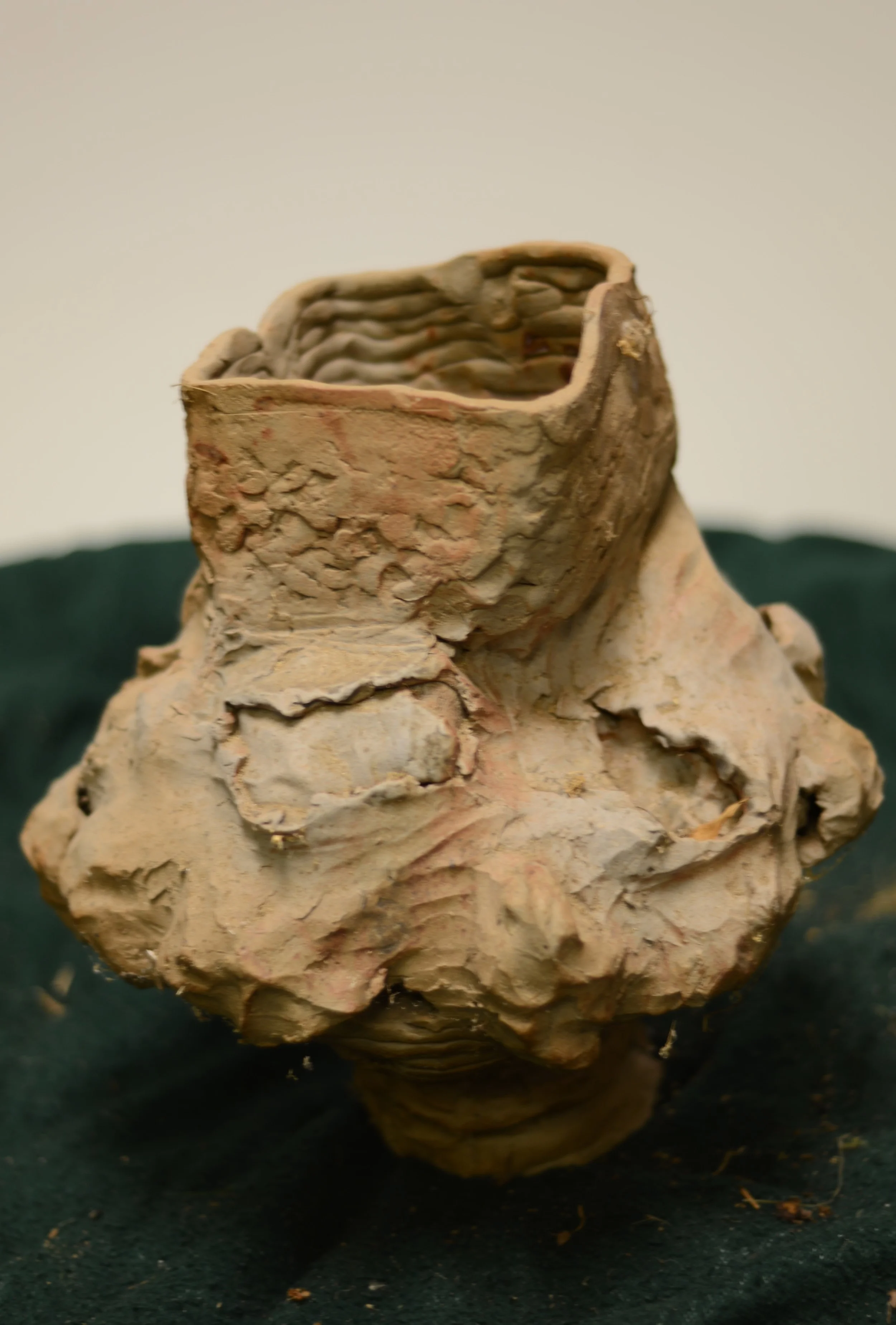 Ancient pottery vessel with intricate ridges and textured surface, placed on a dark fabric background.