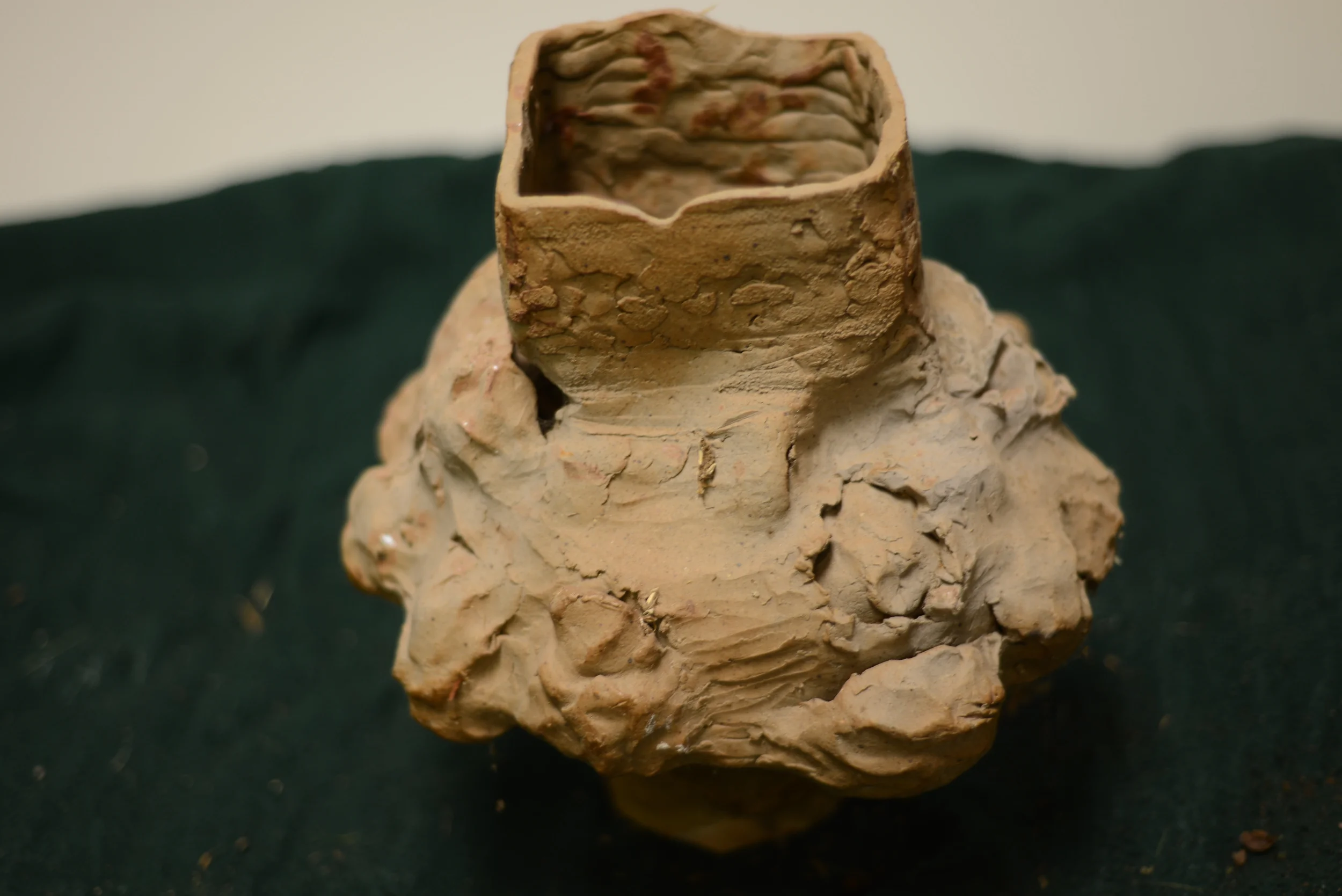 An ancient clay artifact with a square-shaped hollow top, placed on a dark fabric background.