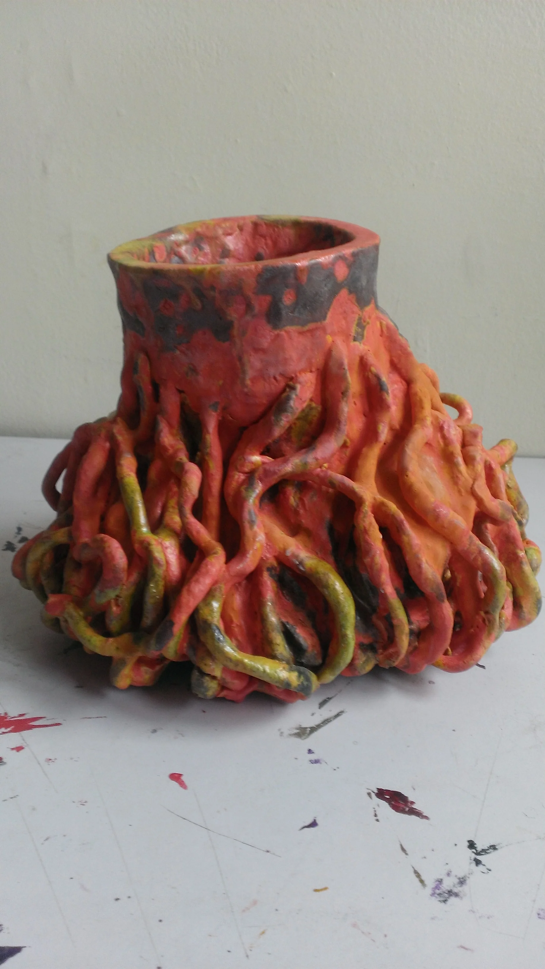 A red and black ceramic sculpture resembling a tree stump with exposed, swirling roots.