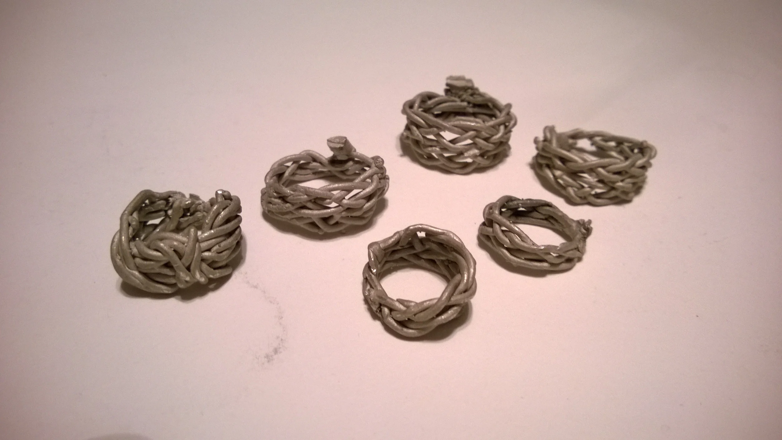 Six small gray woven wire rings arranged on a plain white surface.