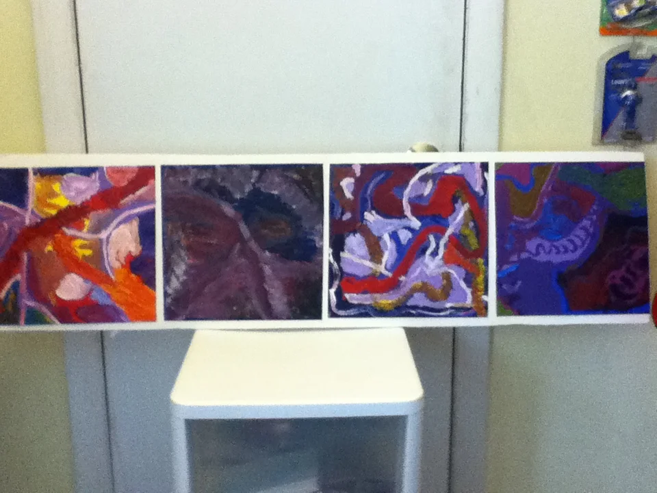A long, horizontal abstract painting with various colorful, swirling patterns and shapes, resting on a table in a room with a refrigerator and some items in the background.