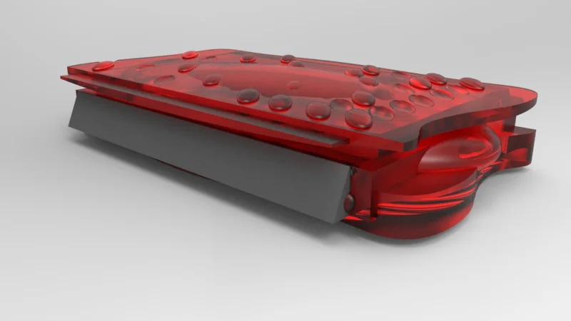 A close-up of a red and gray mechanical device with a transparent red cover and multiple small round protrusions on top, possibly a switch or button system.