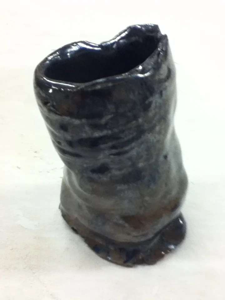 A small ceramic or clay vase with a dark glossy glaze, placed on a white surface.