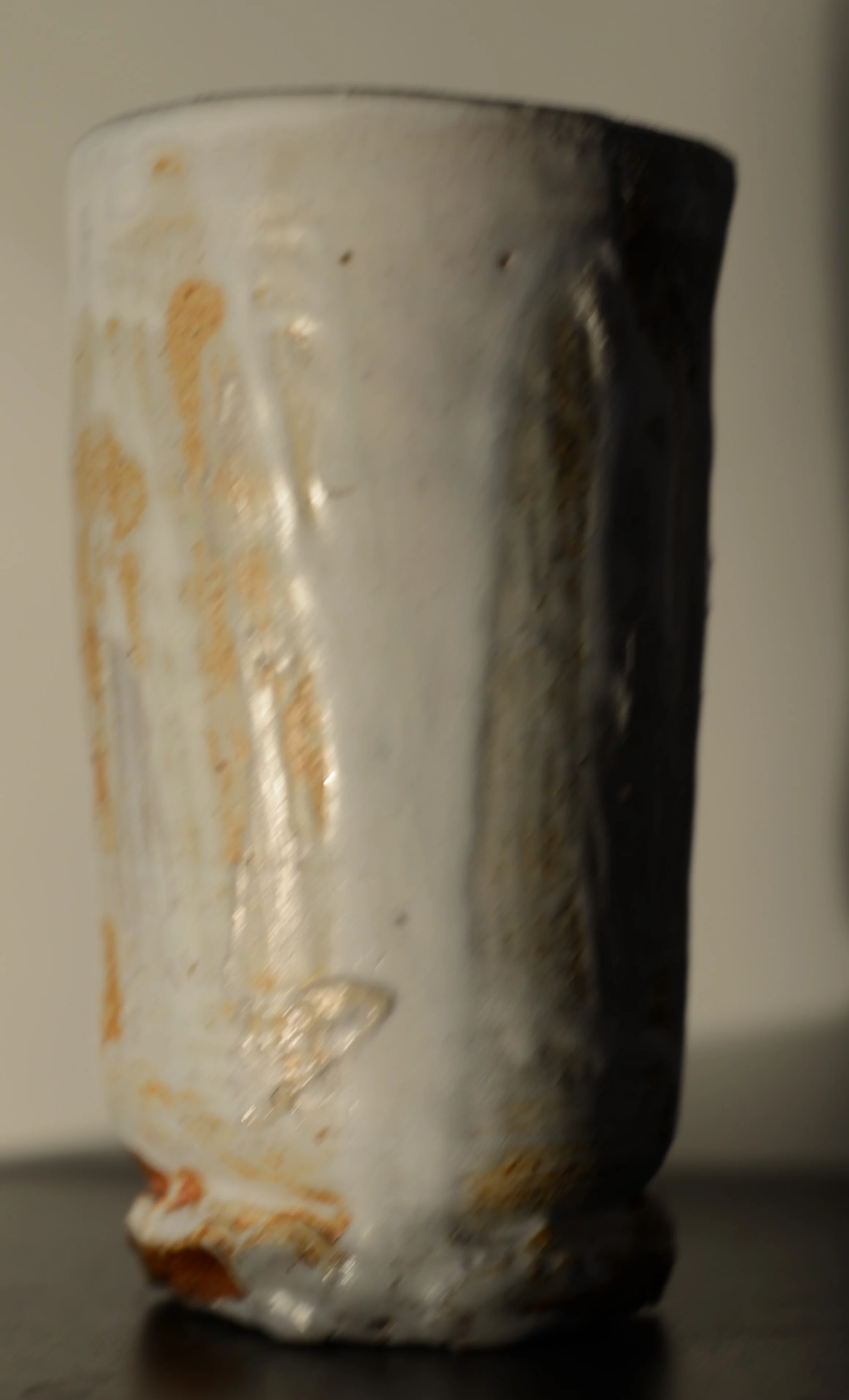 Close-up of a worn, chipped ceramic mug with a light beige and dark brown glaze, placed on a black surface.