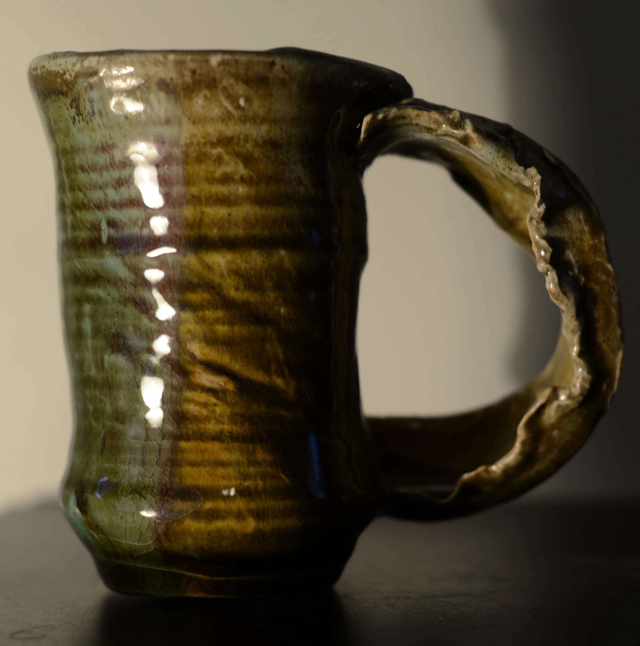 Close-up of a handmade ceramic mug with a textured, glazed surface and a twisted, uneven handle.