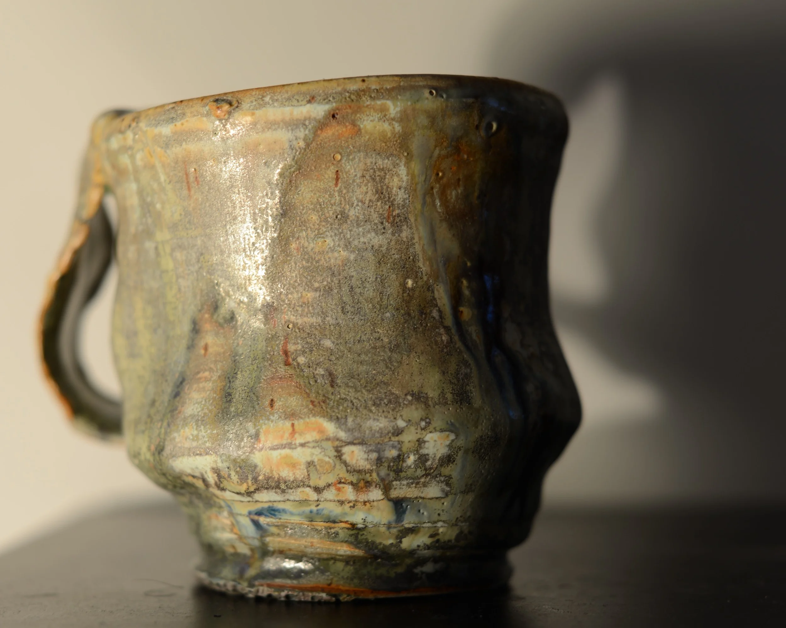 Close-up of a ceramic mug with a textured, multicolored glaze, placed on a dark surface.
