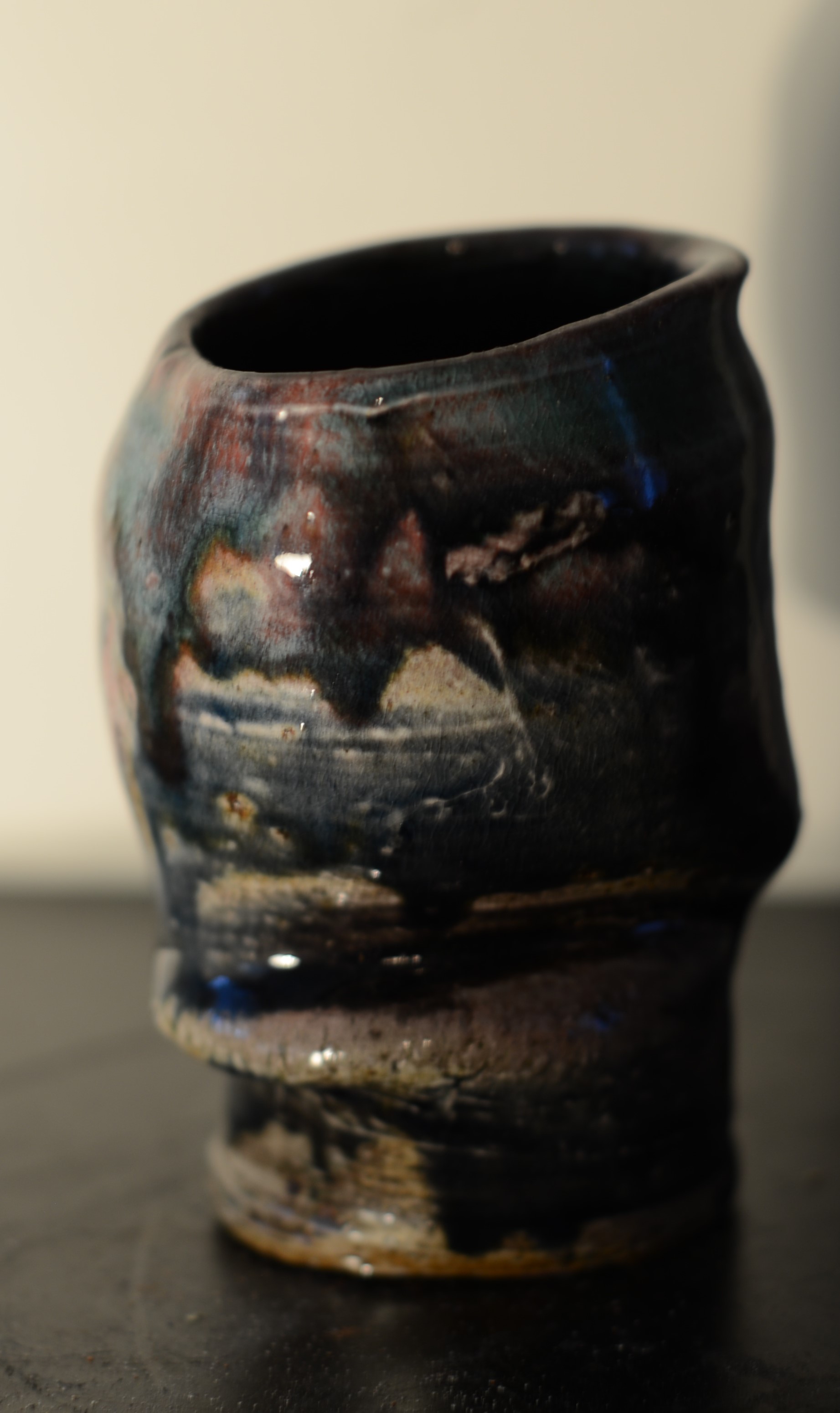 A close-up of a black ceramic vessel with abstract colorful glaze patterns, placed on a dark surface.