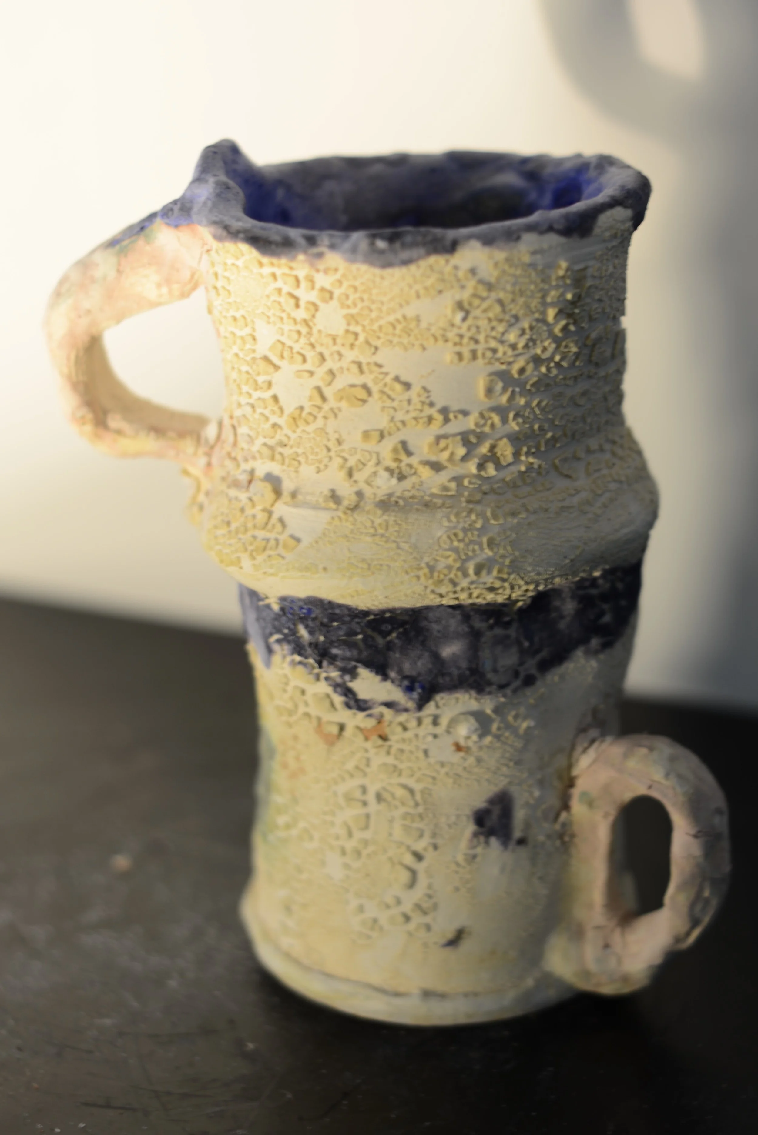 Ceramic mug with textured, perforated surface and two small handles, one on each side.