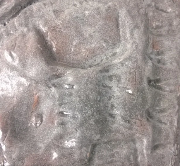 Close-up of a textured stone or concrete surface with indentations and rough patches.
