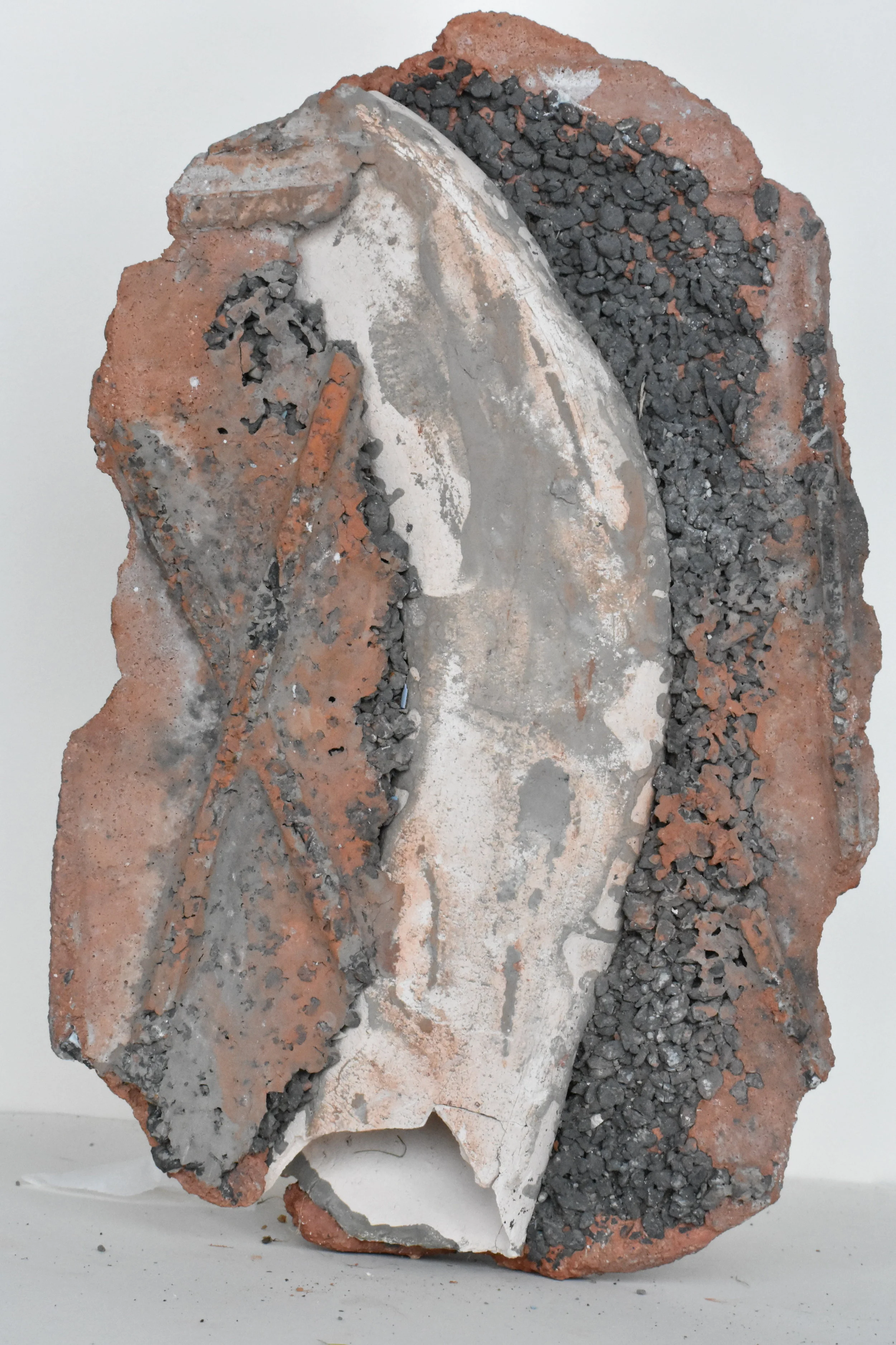 A mixed media sculpture made of broken bricks, concrete, and black gravel, assembled into an abstract shape.