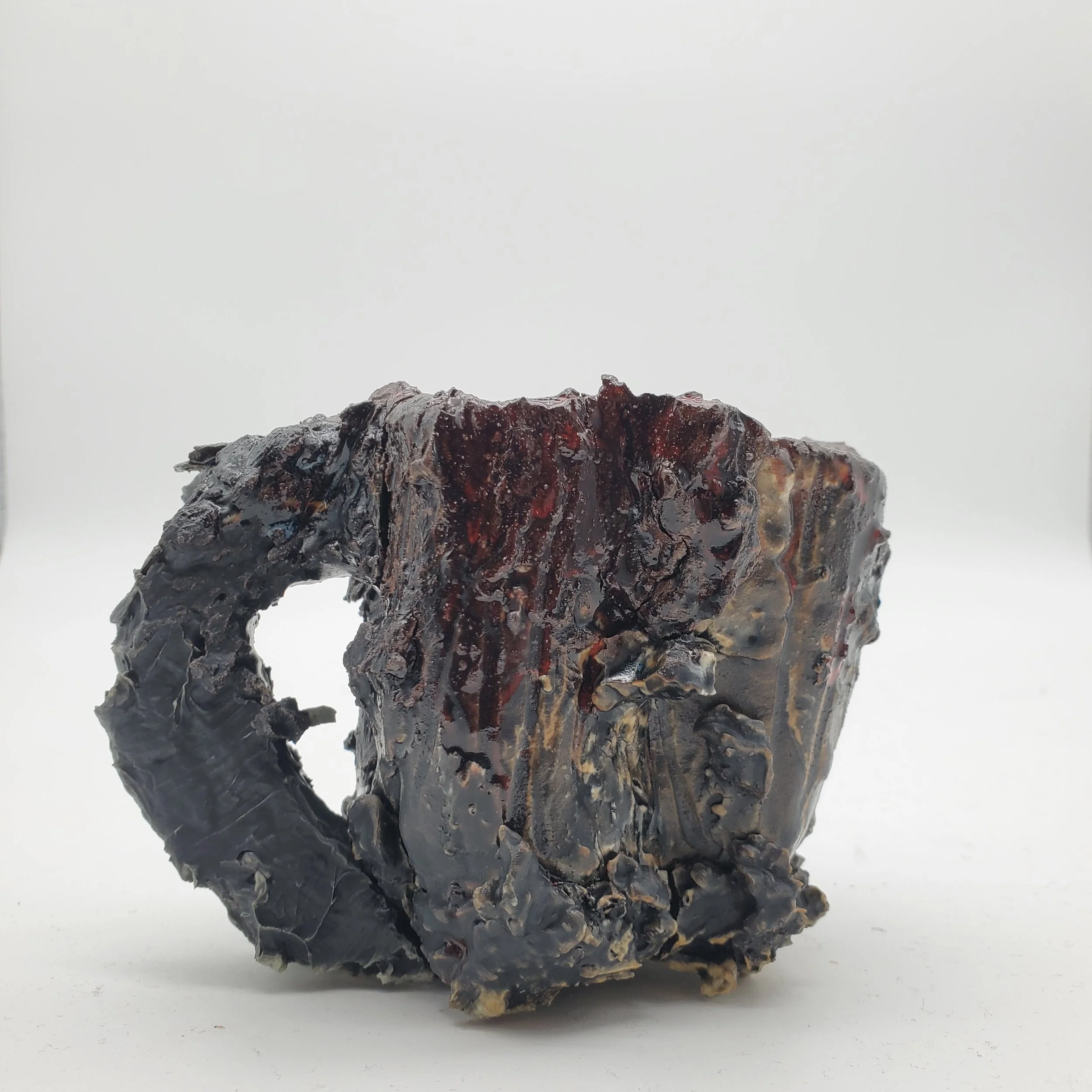 Close-up of a blackened, charred mug with a handle, on a white background.