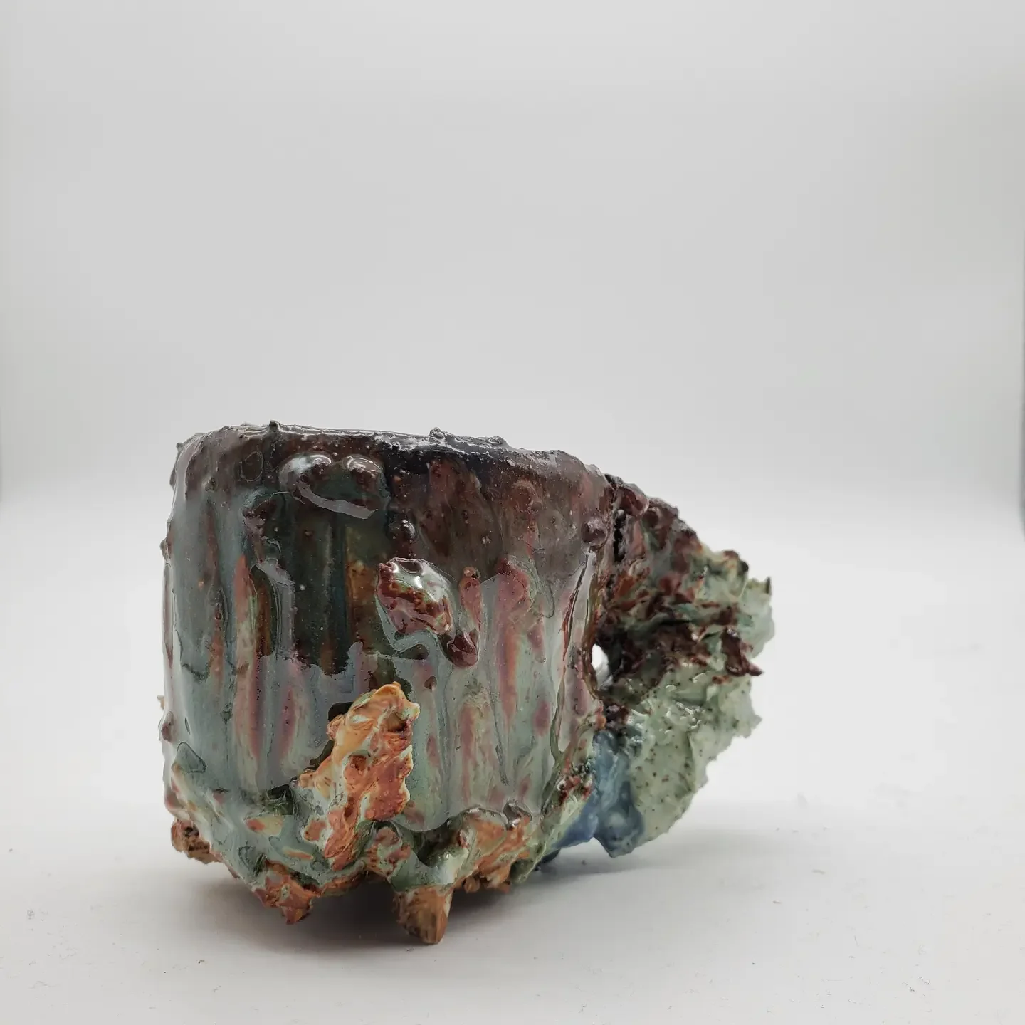 An abstract sculpture with a glossy, multicolored surface, irregular shape, and textured details, set against a plain white background.