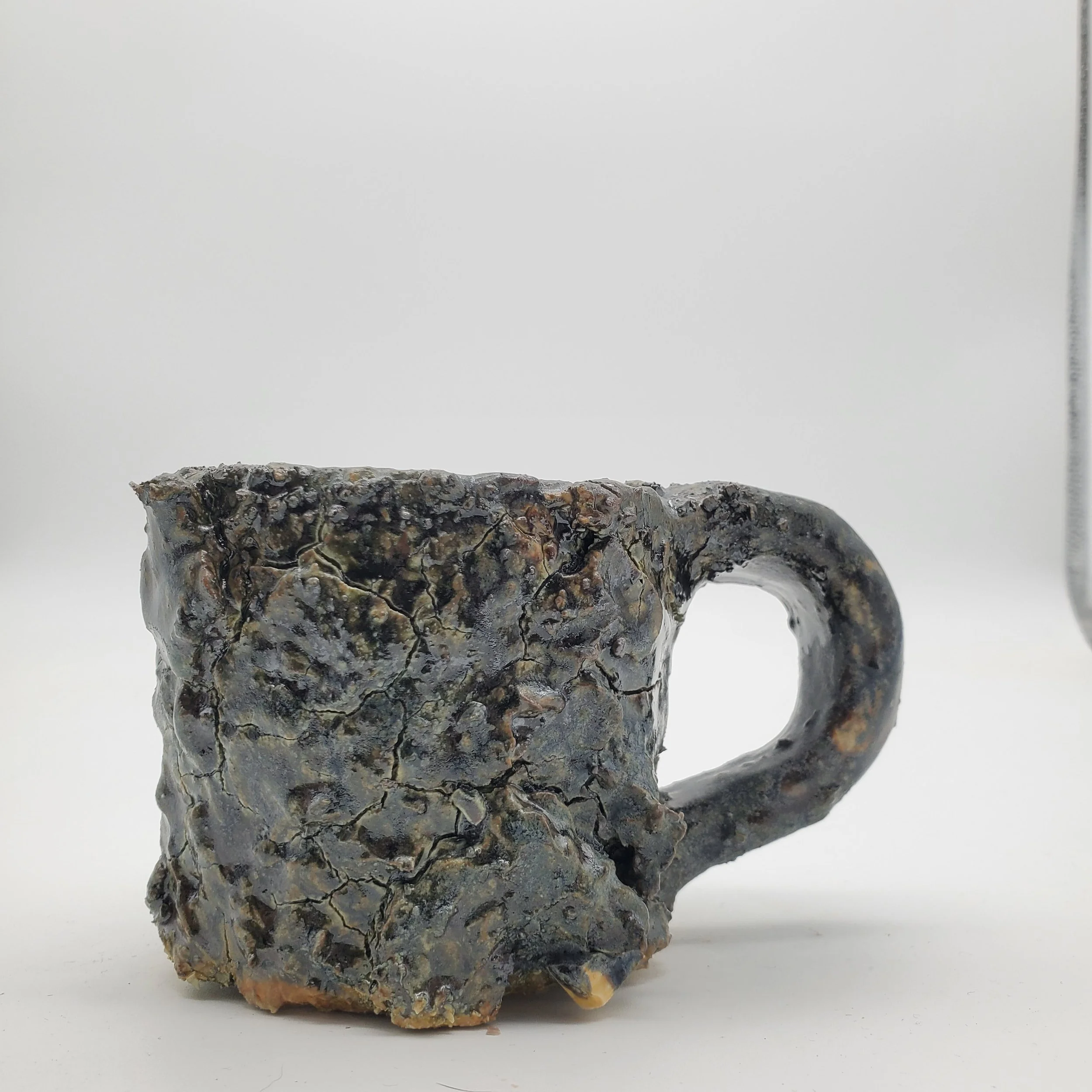 A ceramic mug with a rough, cracked, and textured surface, unglazed and earthy in appearance, set against a plain white background.