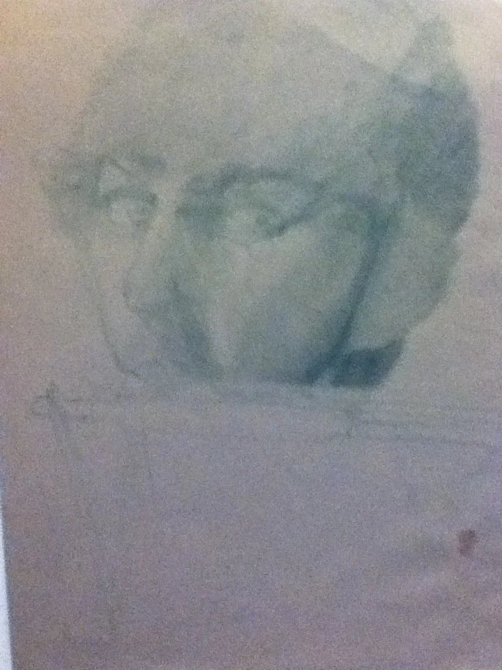 A pencil sketch of a person's face with glasses, appearing to be a young woman with short hair, on a piece of paper.