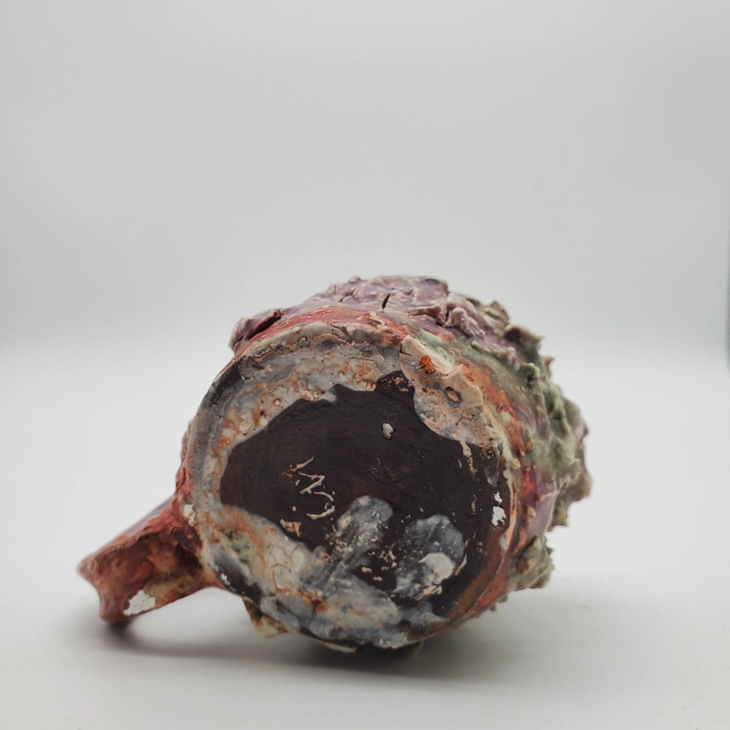 Close-up of a coral-like object with a hollow center and various textures and colors, set against a plain white background.