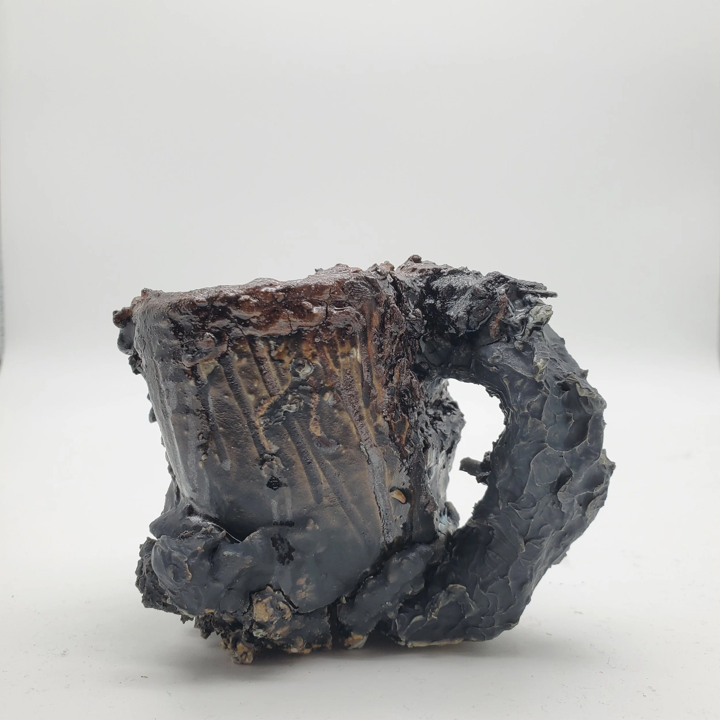A burned, charred coffee mug with a damaged handle against a plain white background.