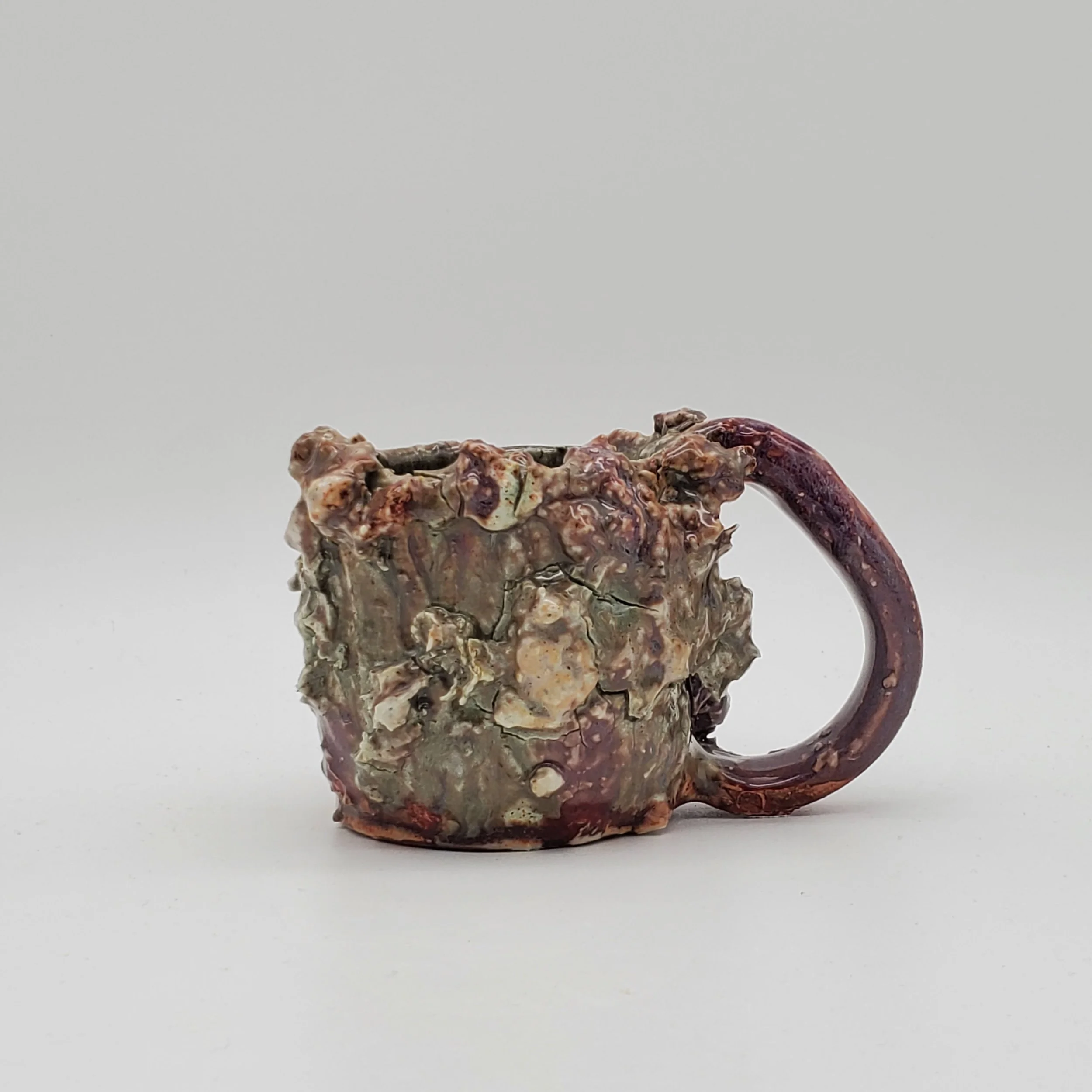 A ceramic coffee mug with a rough, textured surface and a dark red handle, sitting on a plain white background.
