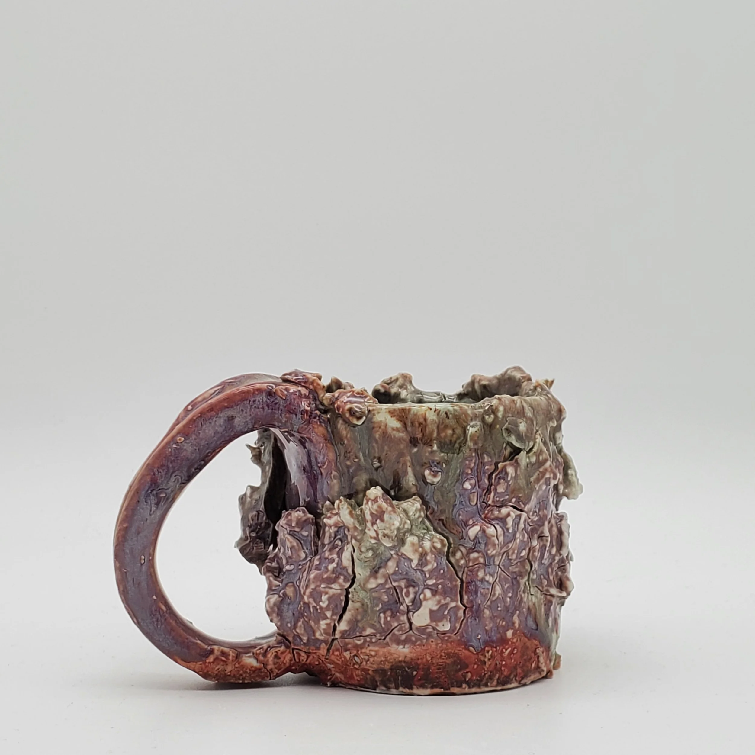 A ceramic mug with a textured, uneven surface and glazed in earthy colors, featuring a handle on the left.