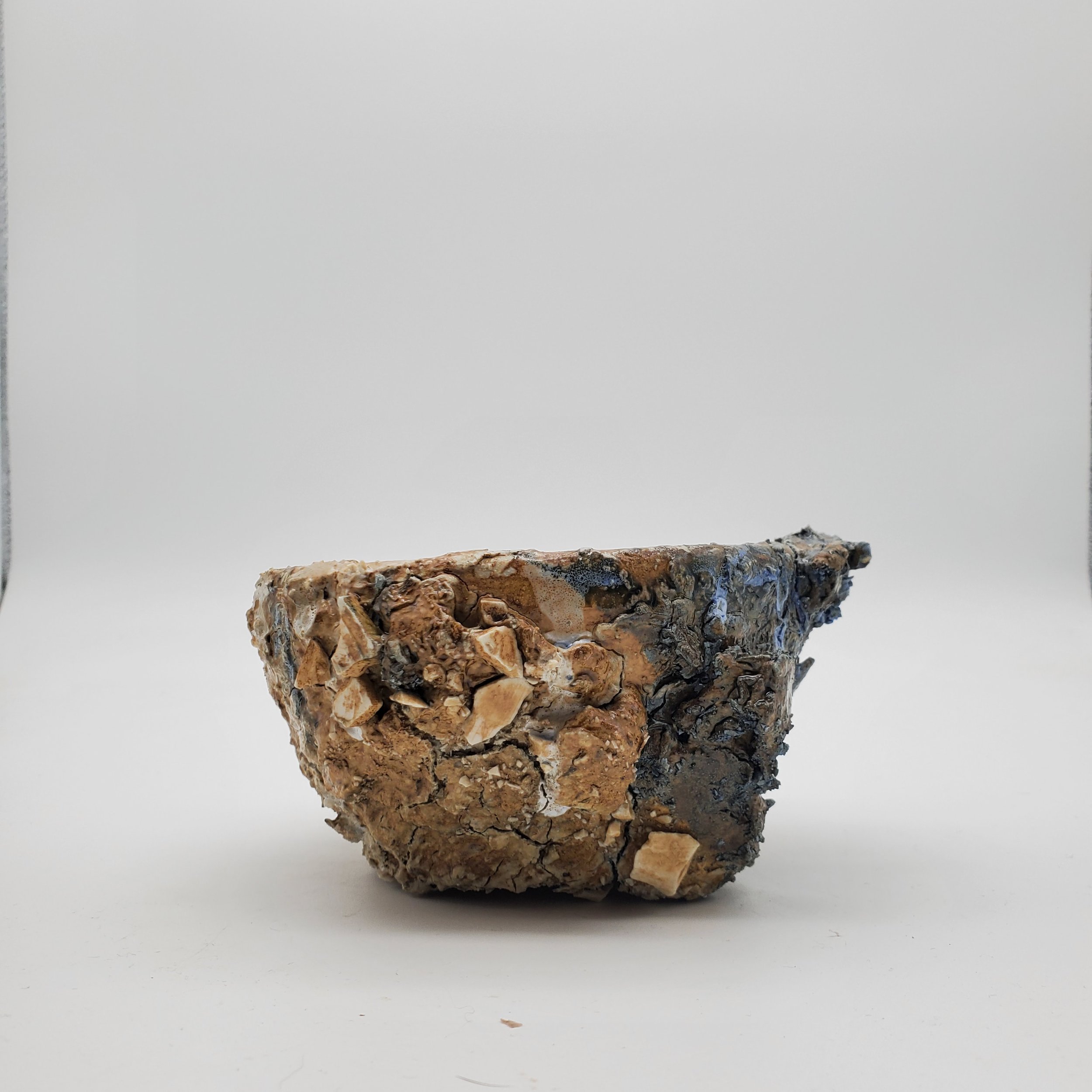 A close-up of a rough-textured, irregularly shaped rock or mineral specimen isolated on a white background.