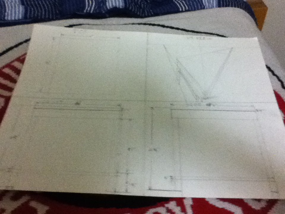 Sketch of a boat with a vertical mast and a long horizontal deck, drawn on a piece of paper placed on a fabric surface.